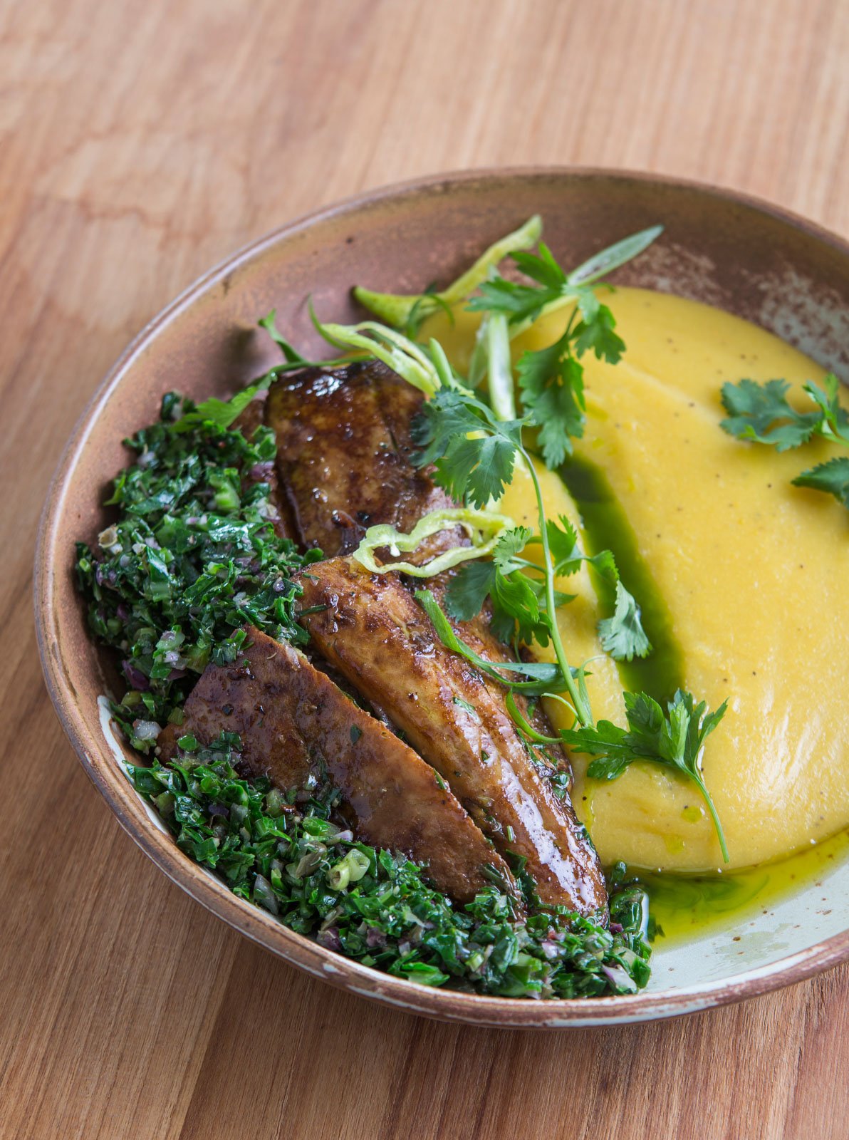A rustic ceramic bowl at Cristalino Jungle Lodge holding caramelised plantain slices, vibrant herb salsa, and a smooth golden purée garnished with fresh coriander