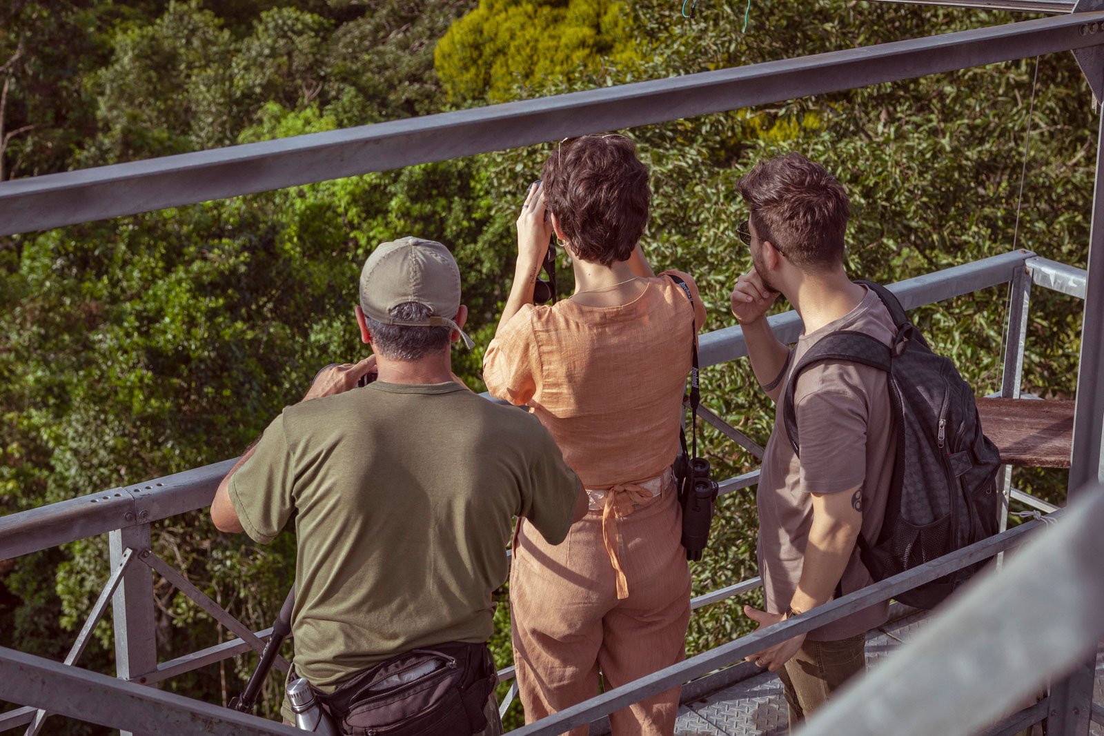 Three visitors scan the rainforest canopy with binoculars from a steel observation tower at Cristalino Jungle Lodge