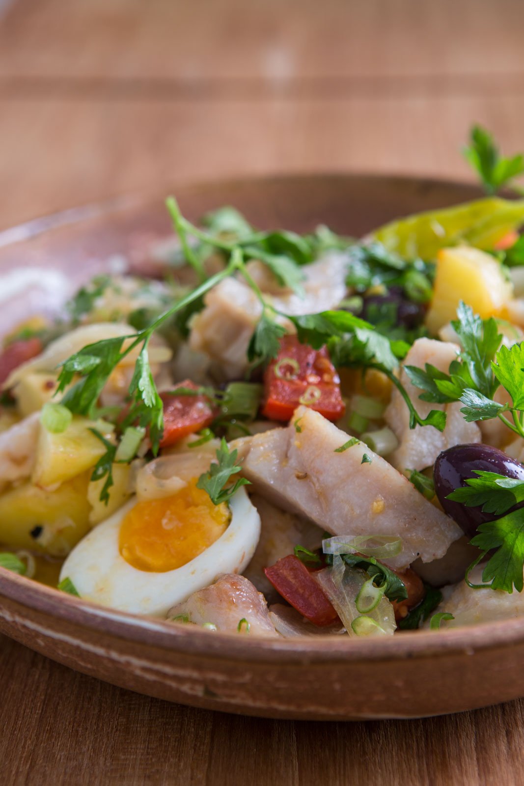 A rustic clay bowl filled with flaked white fish, boiled egg halves, diced yellow potato, black olives, chopped red sausage, spring onion and fresh parsley — a hearty lodge meal at Cristalino Jungle Lodge
