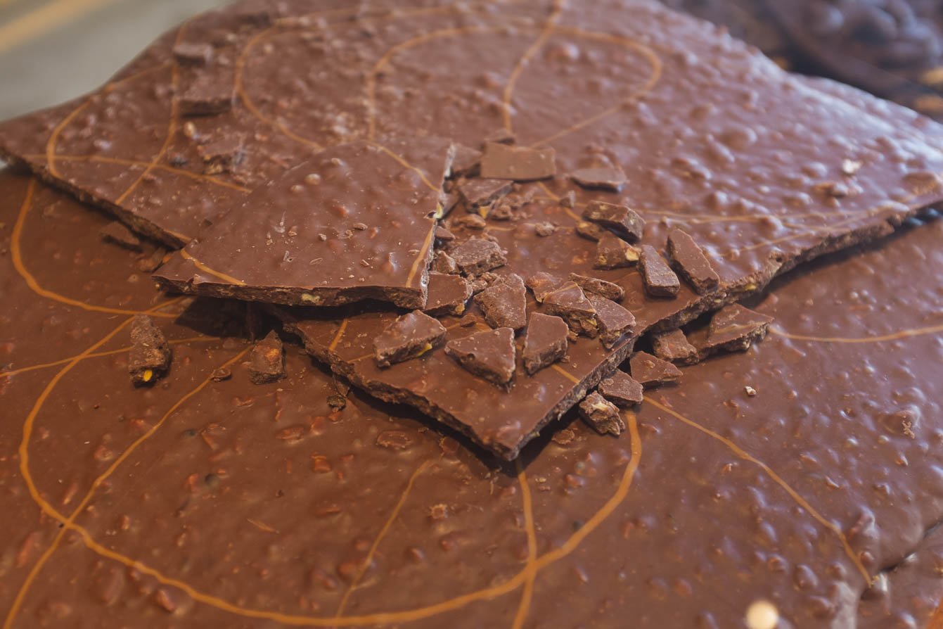 Bean to bar — handcrafted chocolate straight from the Bahian cocoa heartland. Freshly broken slabs of artisan milk chocolate with nut inclusions spread across a marble surface during a cycling Bahia cocoa farm visit