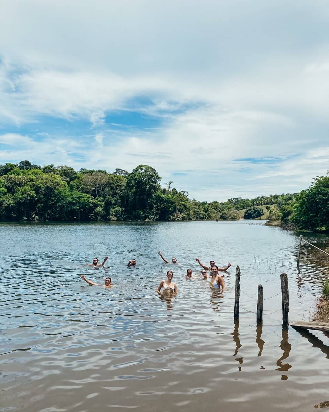 Cool off in a hidden lake deep in the Atlantic Forest — one of those spontaneous moments that make this route unforgettable. A cheerful group of cycling Bahia travelers swimming and waving in a calm lake surrounded by lush Atlantic Forest near Itacaré