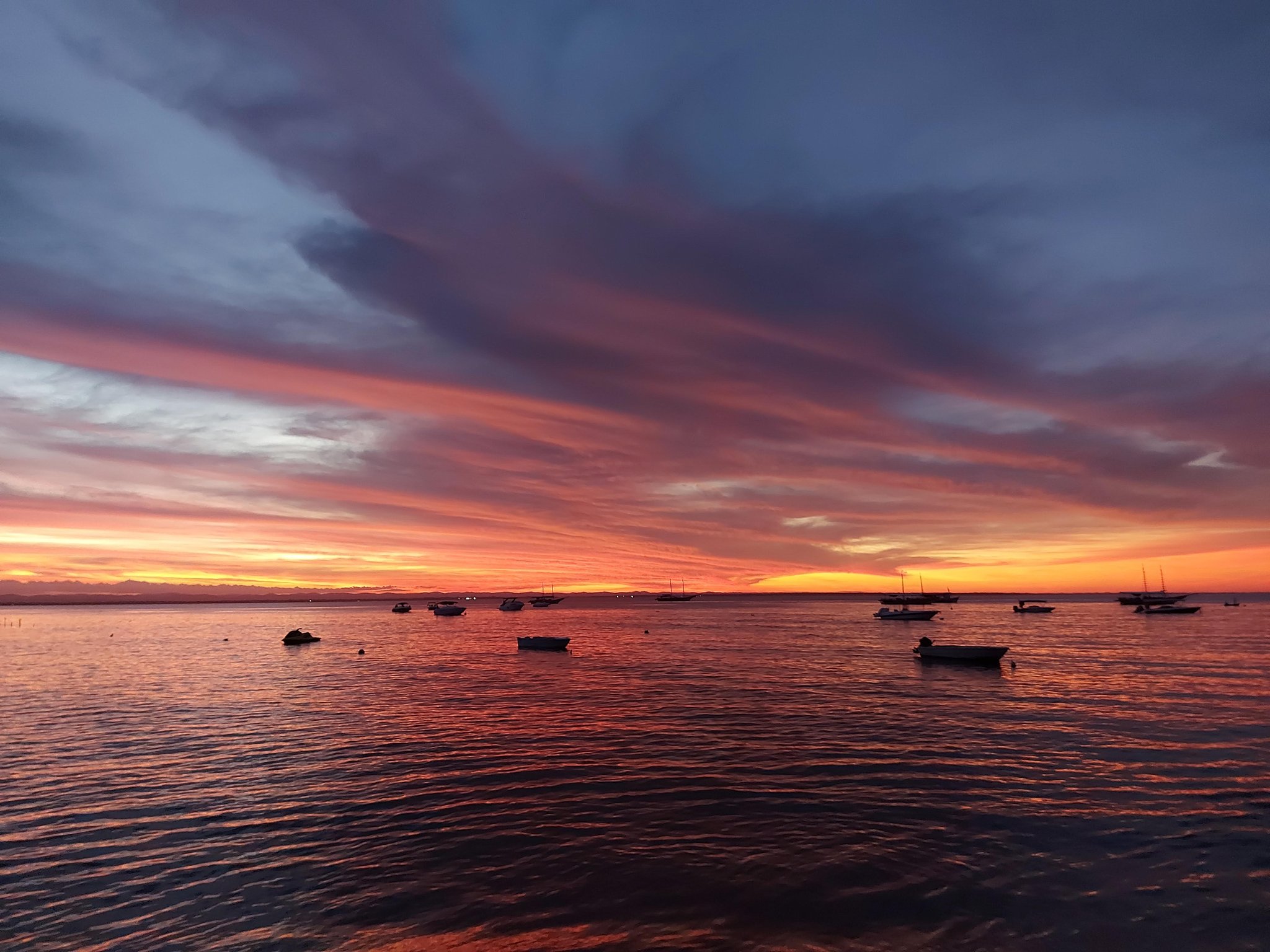 The sky ignites over Itacaré — a perfect close to a day on the saddle. Fiery orange and crimson sunset over Itacaré harbour with silhouetted boats moored on calm water, seen on a cycling Bahia tour