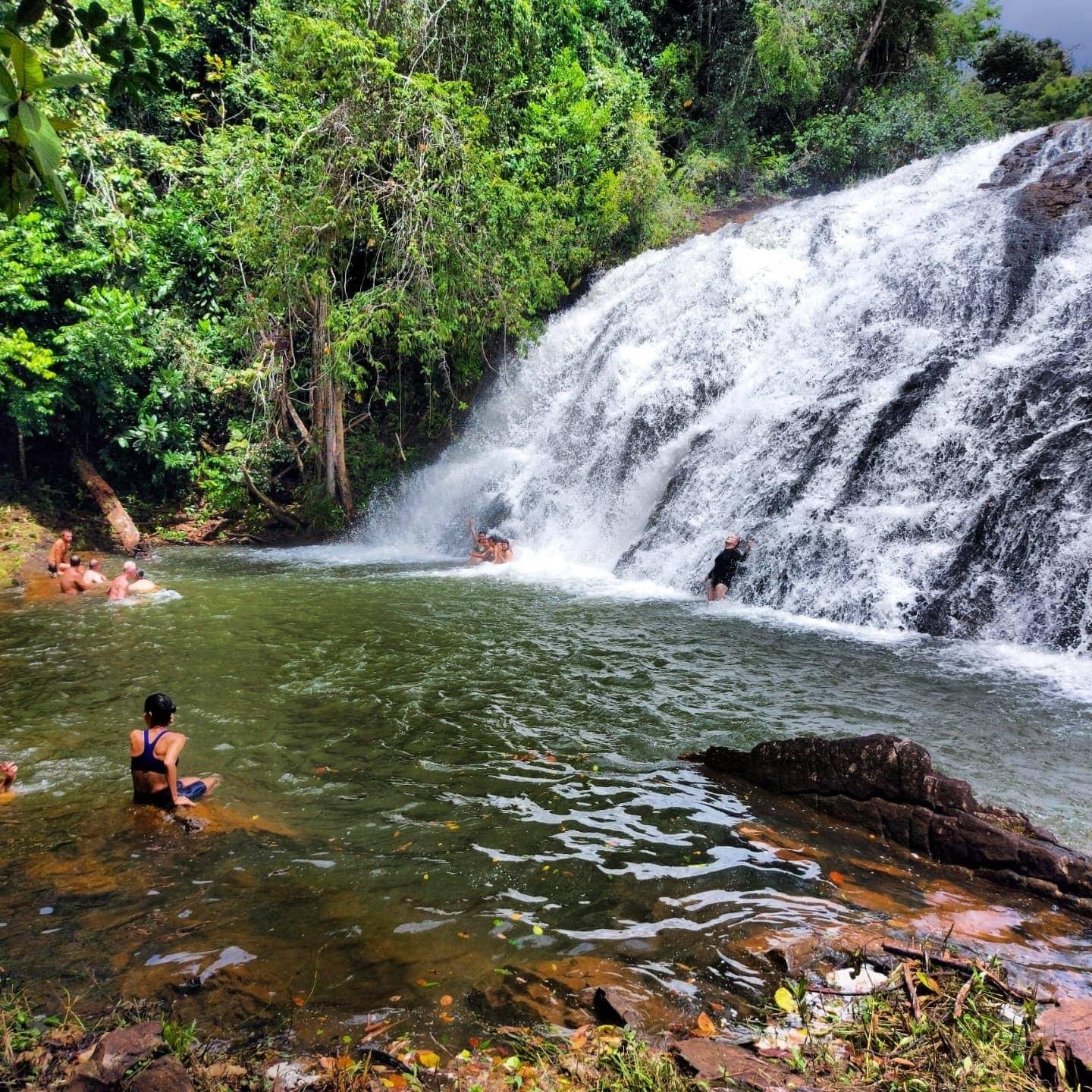 A well-earned plunge — Milagrosa Waterfall rewards the ride. Travellers swimming in the natural pool at Milagrosa Waterfall, surrounded by dense Atlantic Forest on the cycling Bahia Cocoa Route near Serra Grande