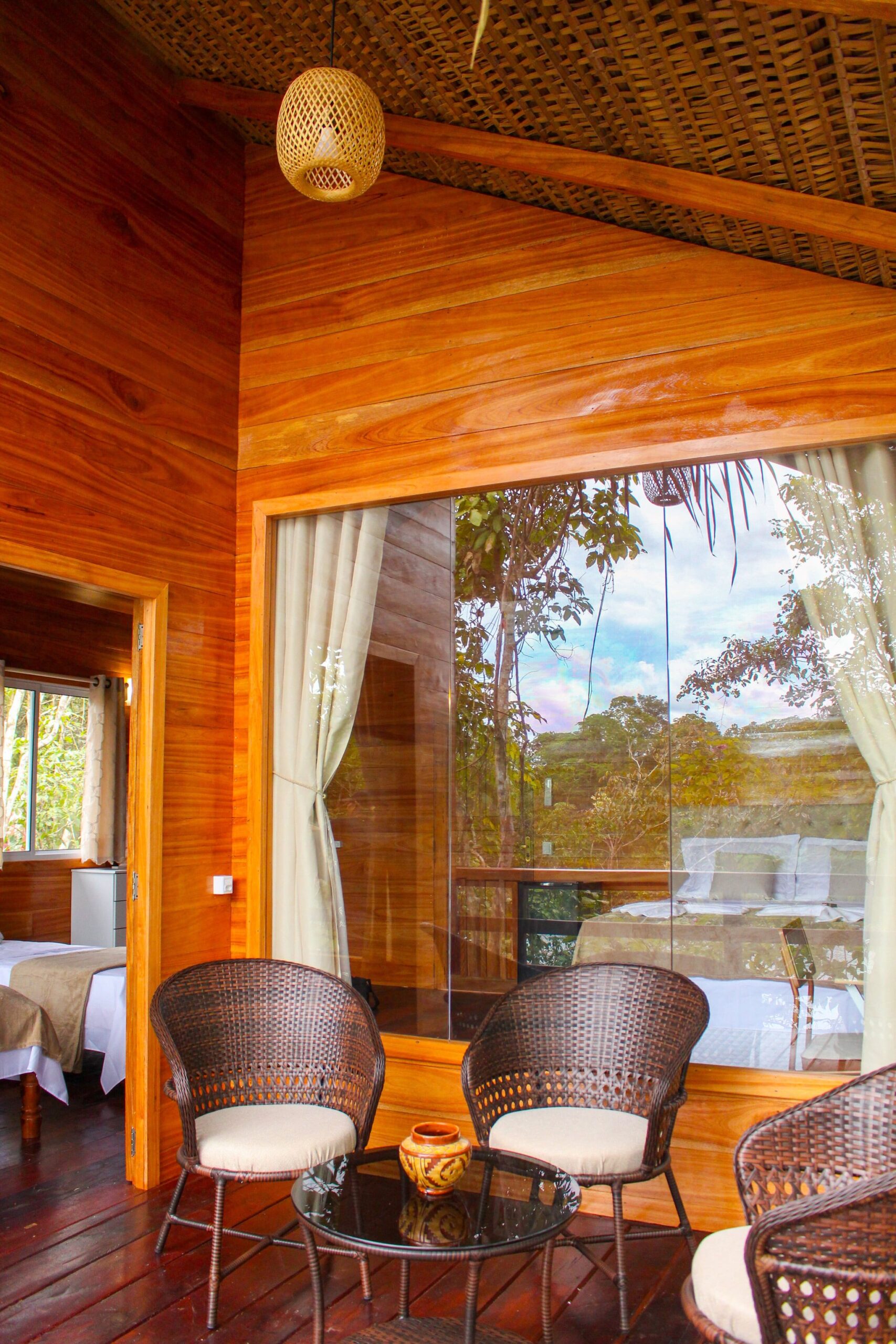 Private wooden balcony at Dolphin Lodge with rattan armchairs and a glass wall onto the forest