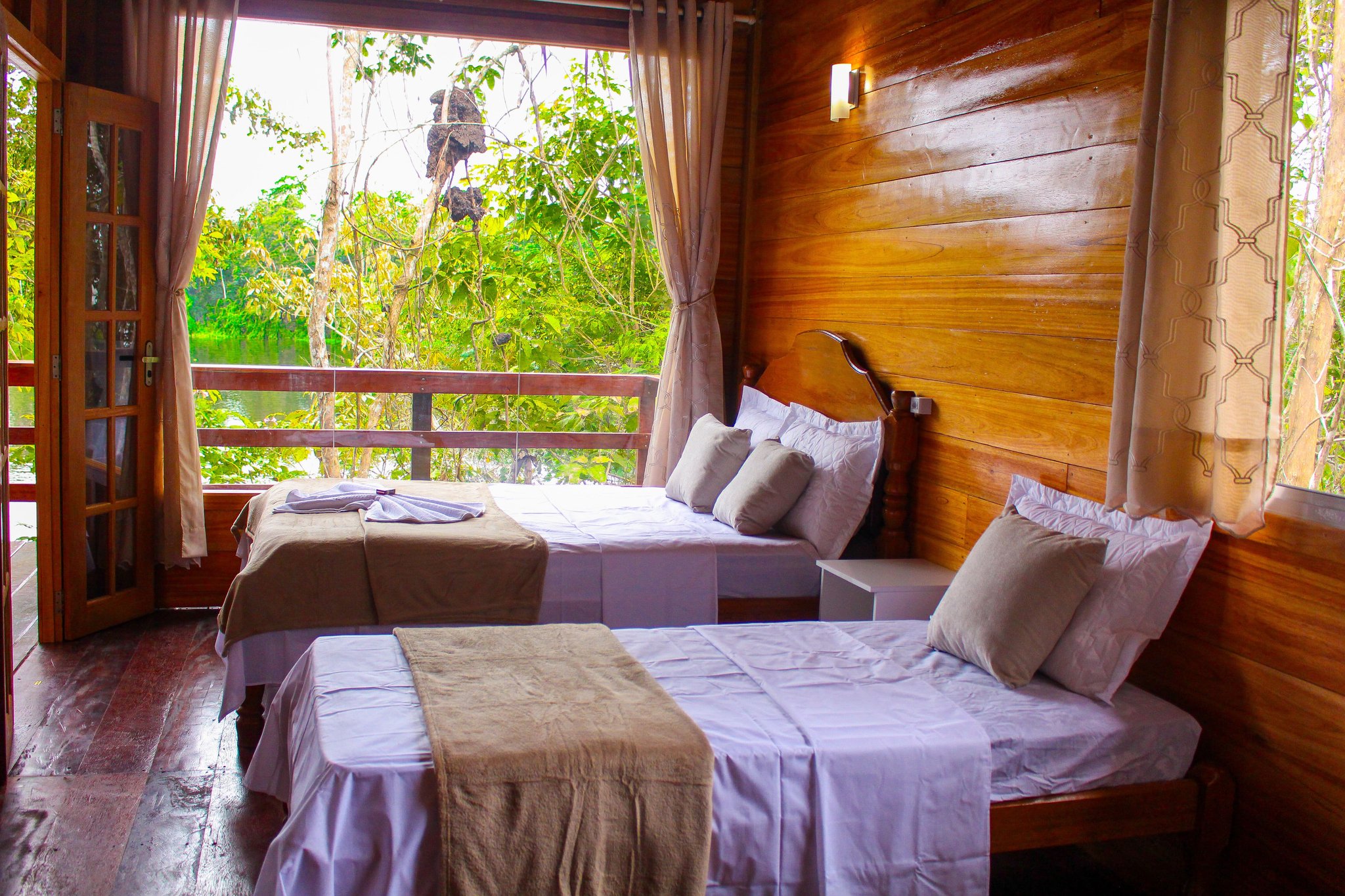 Dolphin Lodge twin bedroom with two beds and a balcony framing a leafy jungle view
