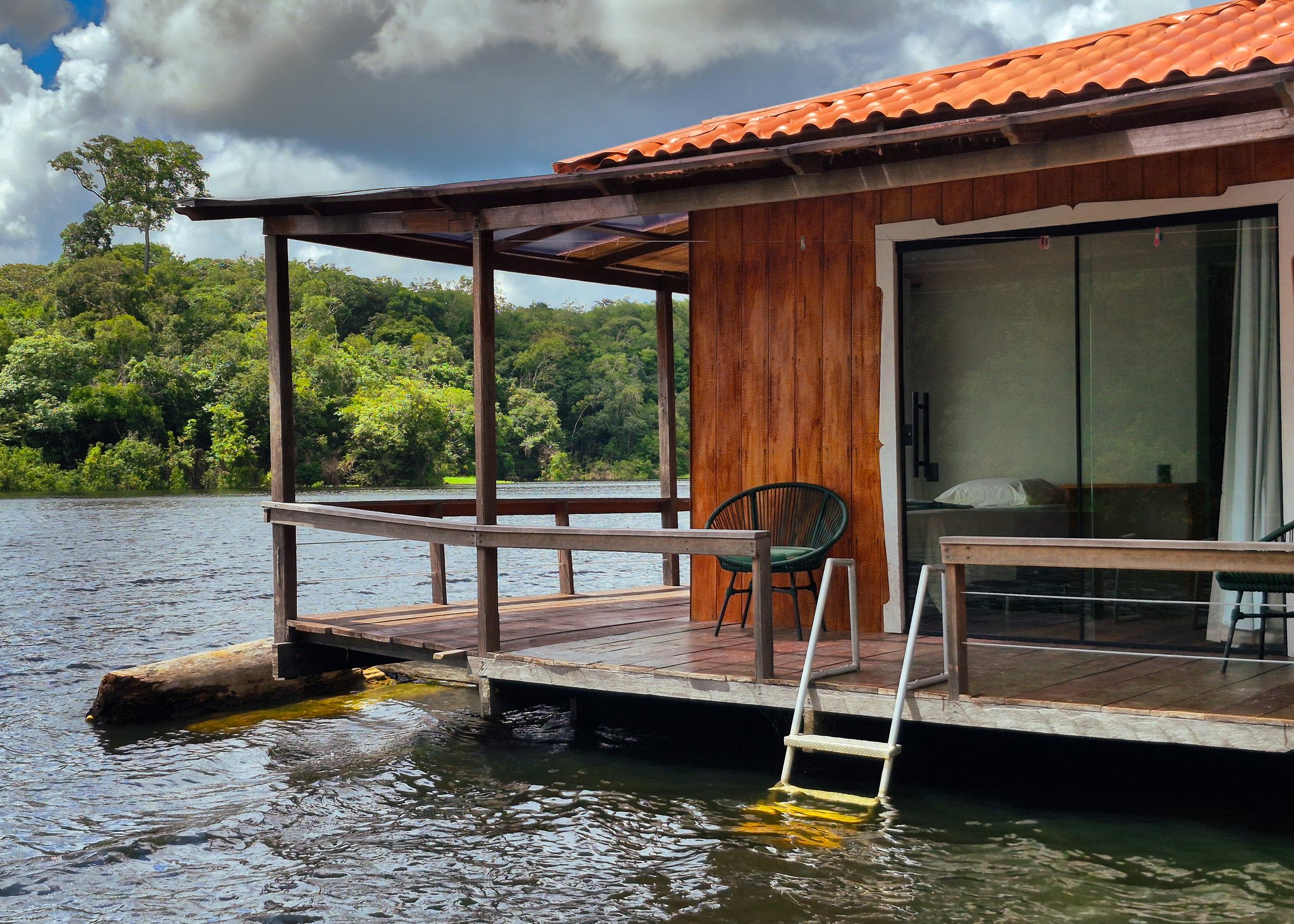 Private covered deck of an Eco Floating Lodge bungalow with chairs and a ladder over the river