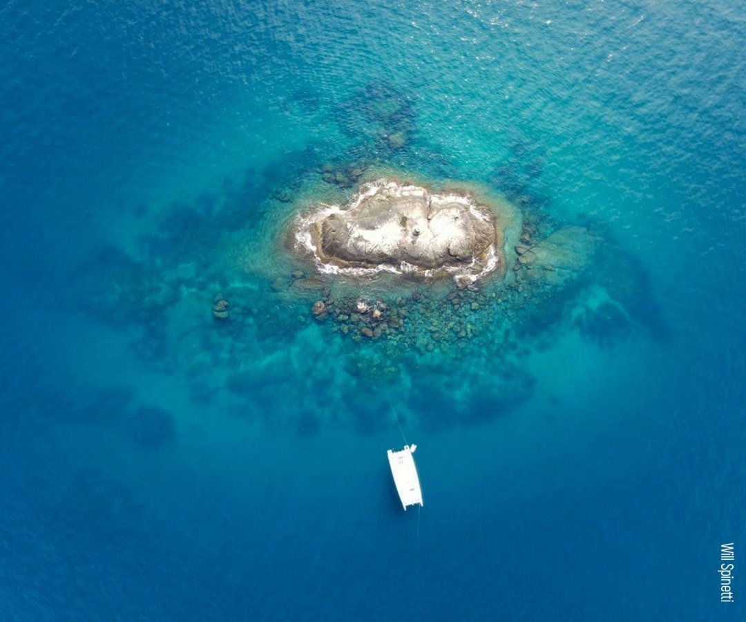 Aerial view of a white catamaran anchored beside a rocky islet surrounded by crystal-clear turquoise water on a Fernando de Noronha diving trip
