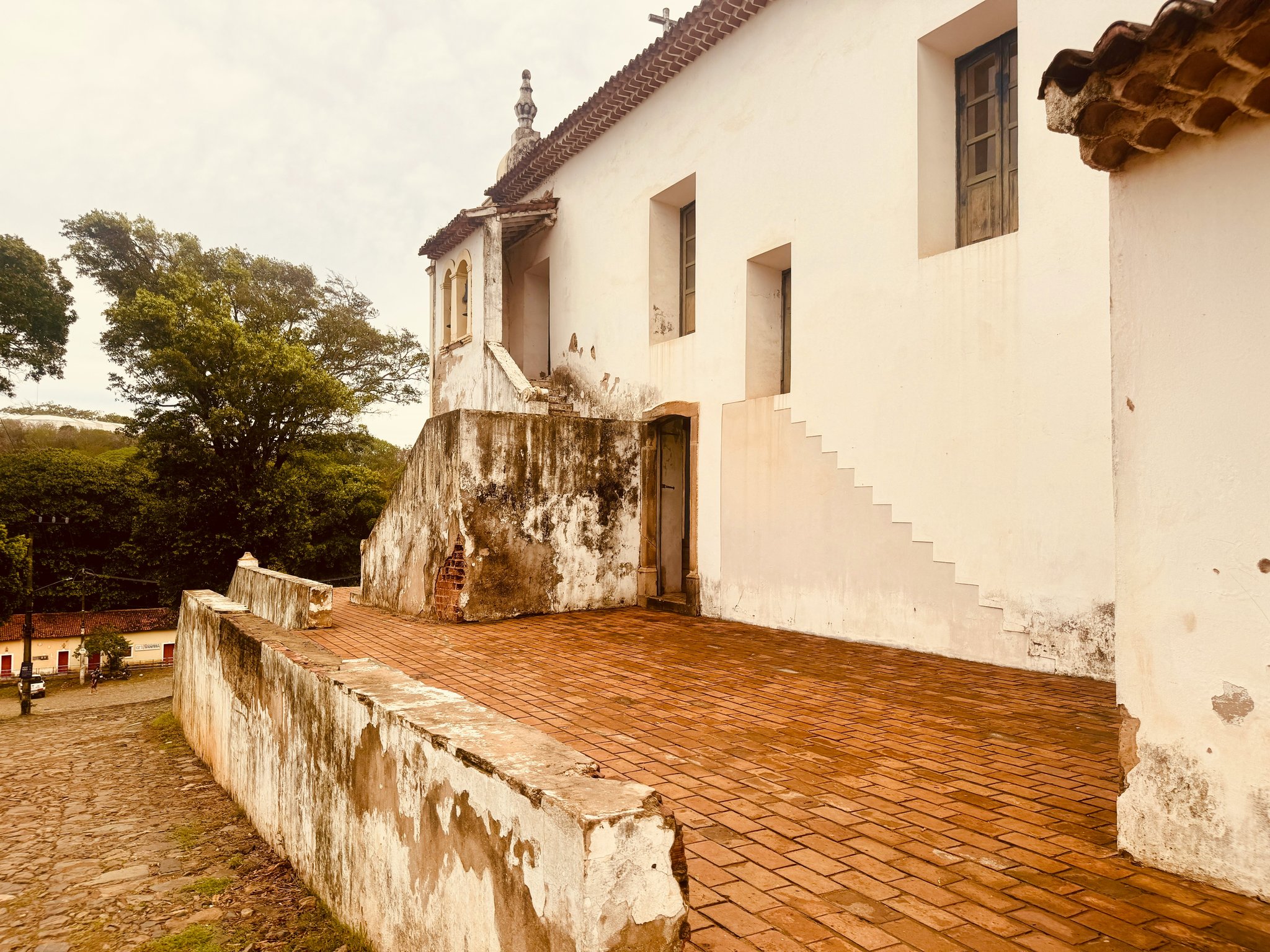 Weathered white colonial church facade with terracotta brick terrace and bell tower overlooking a cobblestone square in Fernando de Noronha Brazil