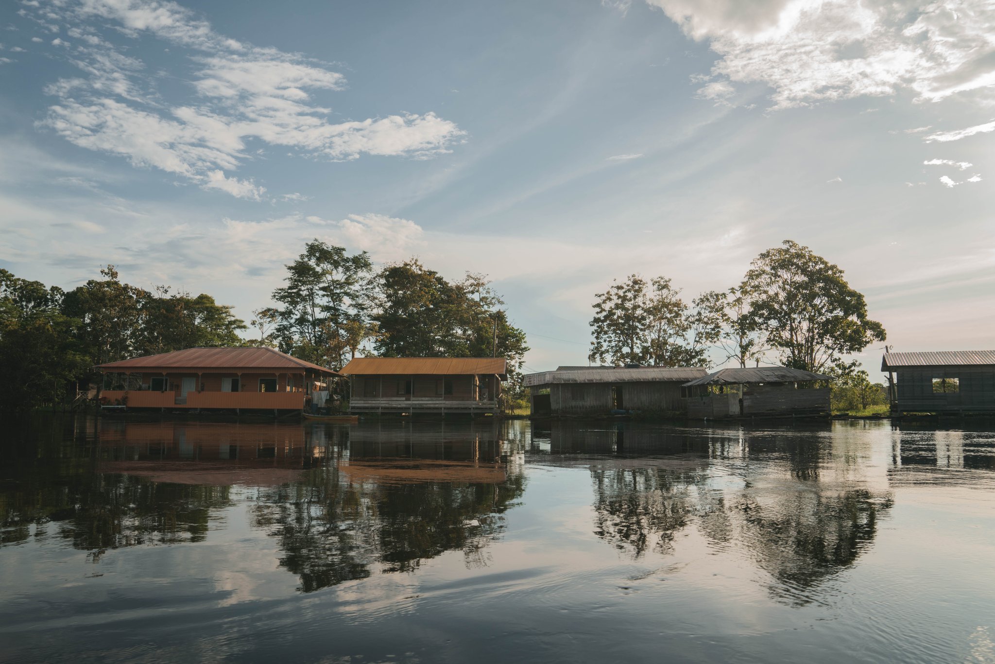 Floating homes line the river, mirrored on its glassy surface. Photo: Yuri Panichi Floating river houses reflected on the calm water under a wide Amazon sky