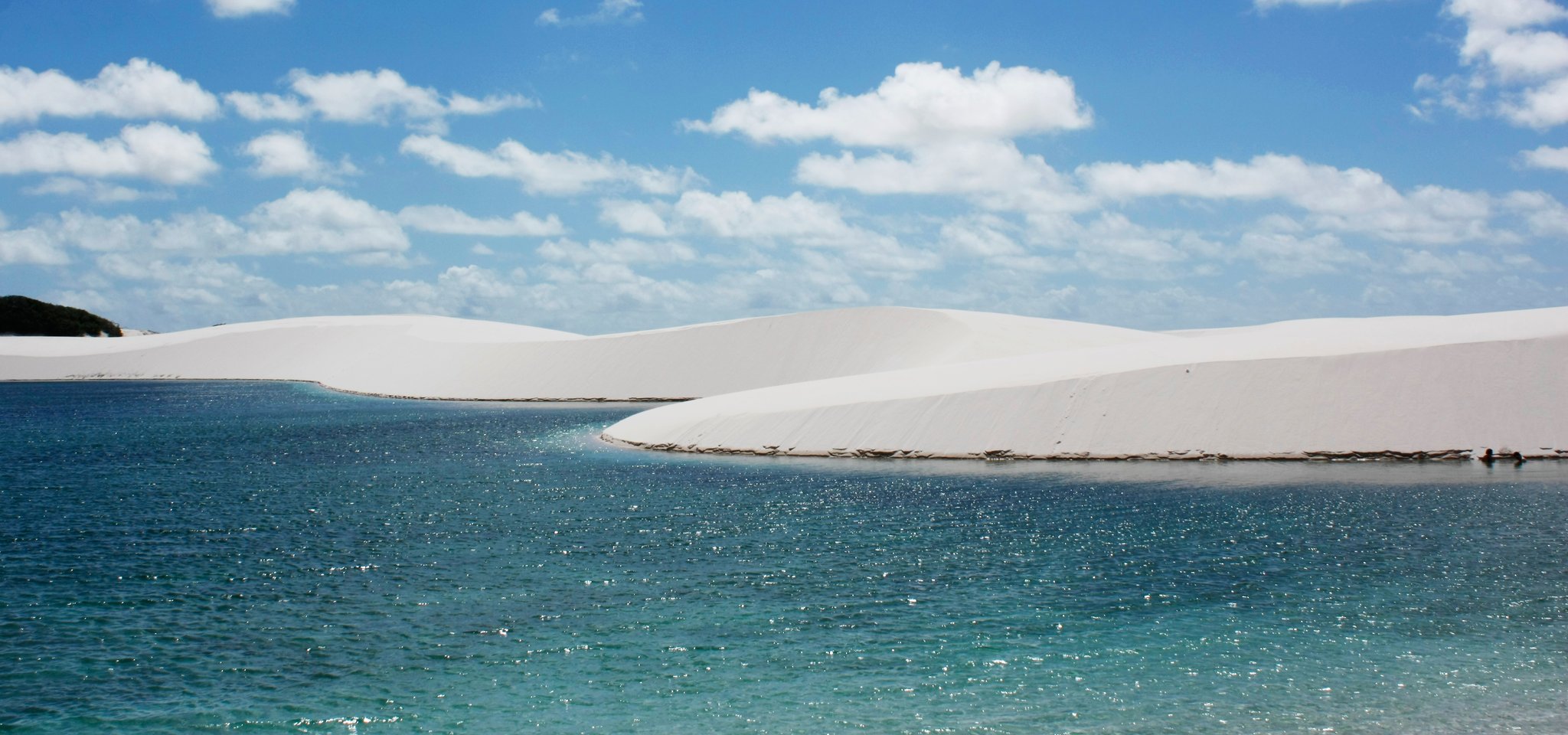 Blue water, white sand, endless sky — the lagoons that await between dune crossings. Crystal-clear blue lagoon reflecting a brilliant sky, framed by sweeping white sand dunes — the iconic landscape of the horseback riding Lençóis Maranhenses tour