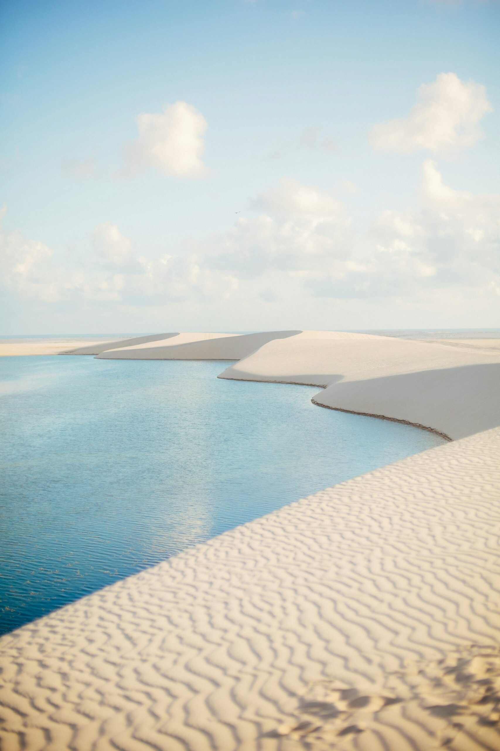 Crystal water carving its way between mountains of white sand — this is the Lençóis Maranhenses at its most surreal. Turquoise rainwater lagoon nestled between sweeping white sand dunes under a soft blue sky in Lençóis Maranhenses, a highlight of the horseback riding Lençóis Maranhenses tour