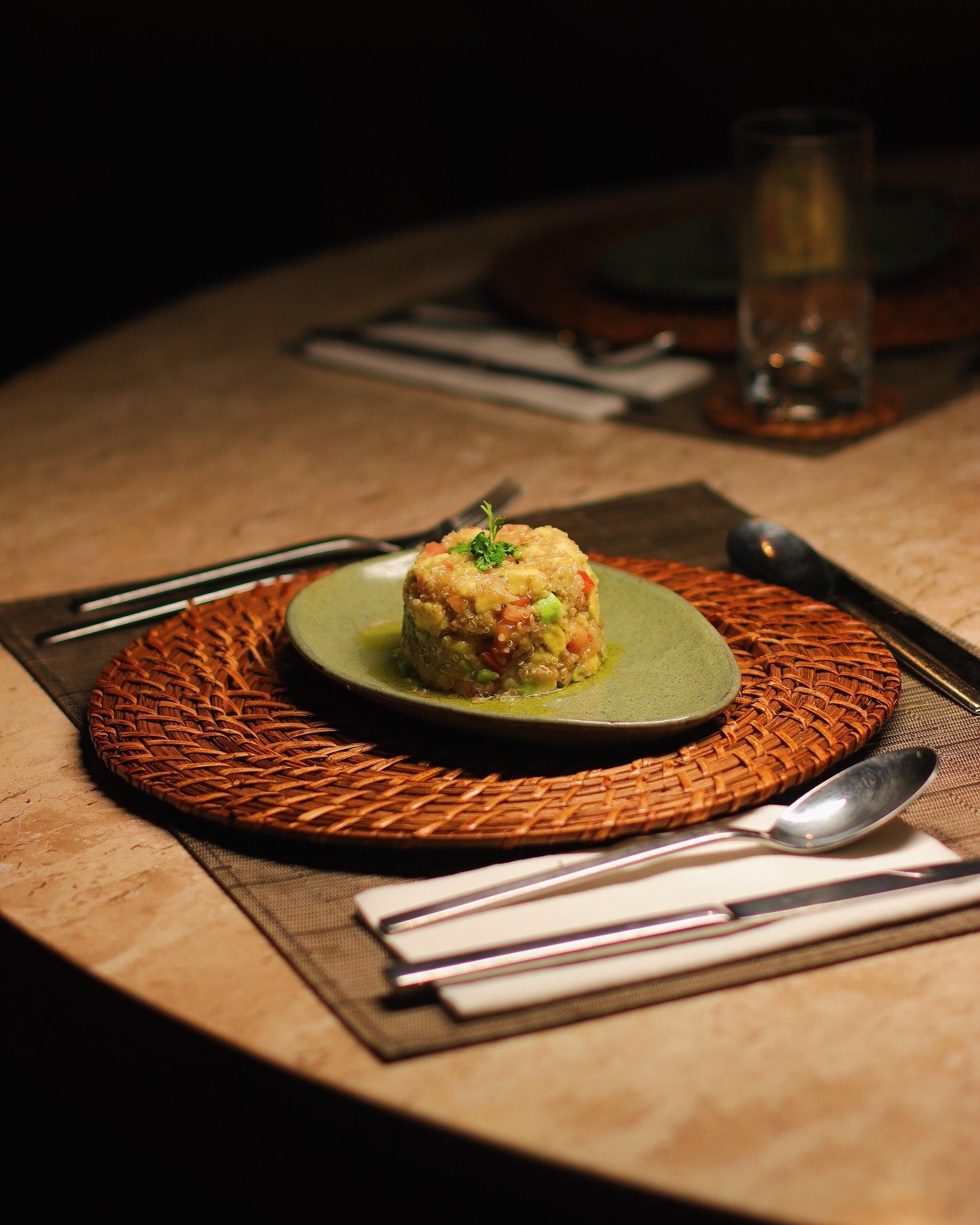 Rainforest dining, plated with care — fresh ingredients, bold colour. A moulded grain and vegetable dish garnished with fresh herbs, served on a green ceramic plate atop a woven rattan charger at Juma Amazon Jungle Lodge