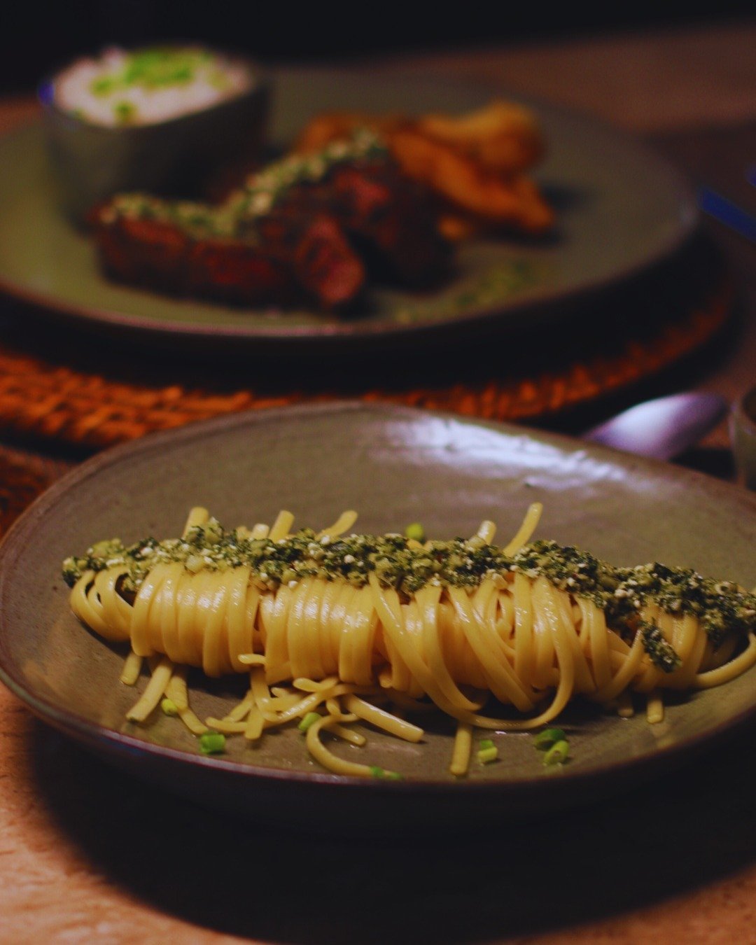 Fresh ingredients, traditional recipes — dinner served nightly at the lodge. A nest of linguine-style pasta topped with herb and seed crumble served on a rustic ceramic plate at Juma Amazon Jungle Lodge, with a plate of grilled meat blurred in the background