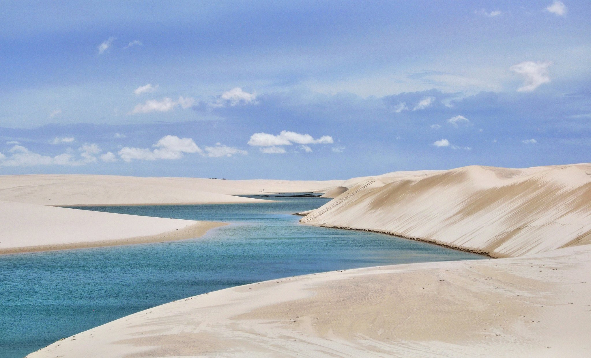 Impossibly blue water pooled between walls of white sand — this is Lençóis Maranhenses at its most surreal. Turquoise rainwater lagoon nestled between sweeping white sand dunes under a blue sky in Lençóis Maranhenses National Park, a defining image of the Lençóis Maranhenses full itinerary