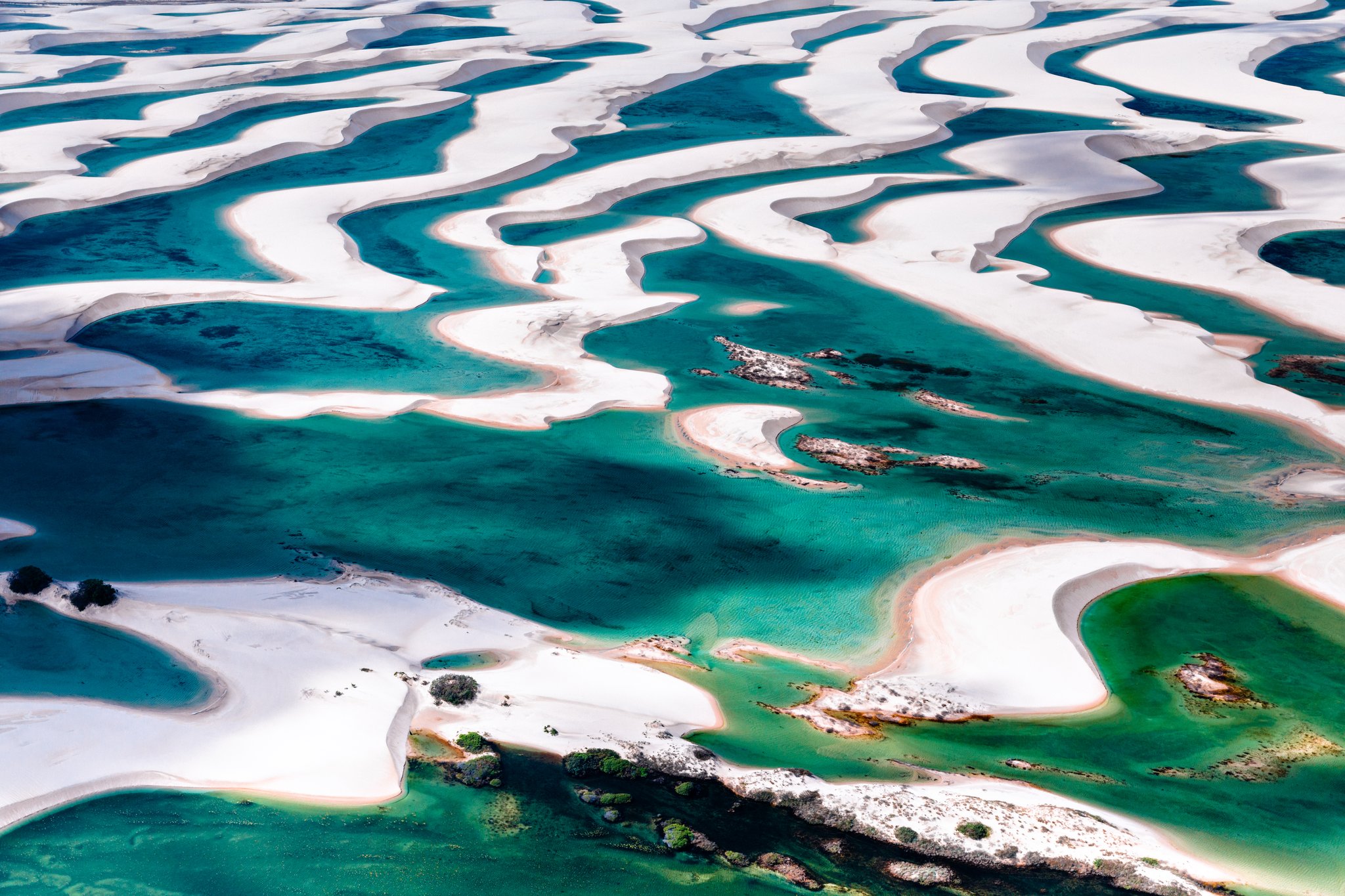 Aerial view of the Lençóis Maranhenses hike landscape, showing sweeping white sand dunes interlaced with vivid turquoise and emerald freshwater lagoons stretching to the horizon