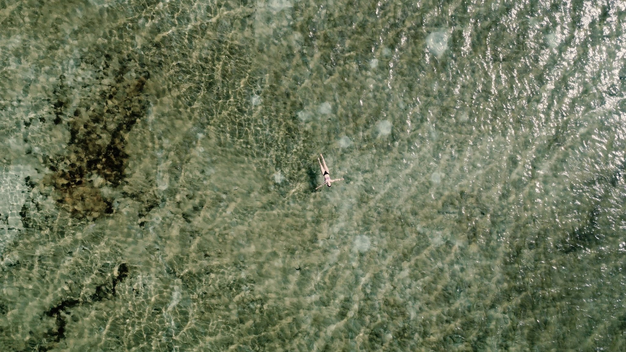 Tiny and weightless, adrift in a lagoon that seems to have no bottom. Aerial view of a lone swimmer floating in the crystal-clear shallow waters of a Lençóis Maranhenses hike lagoon, the sandy bed visible through the glassy surface