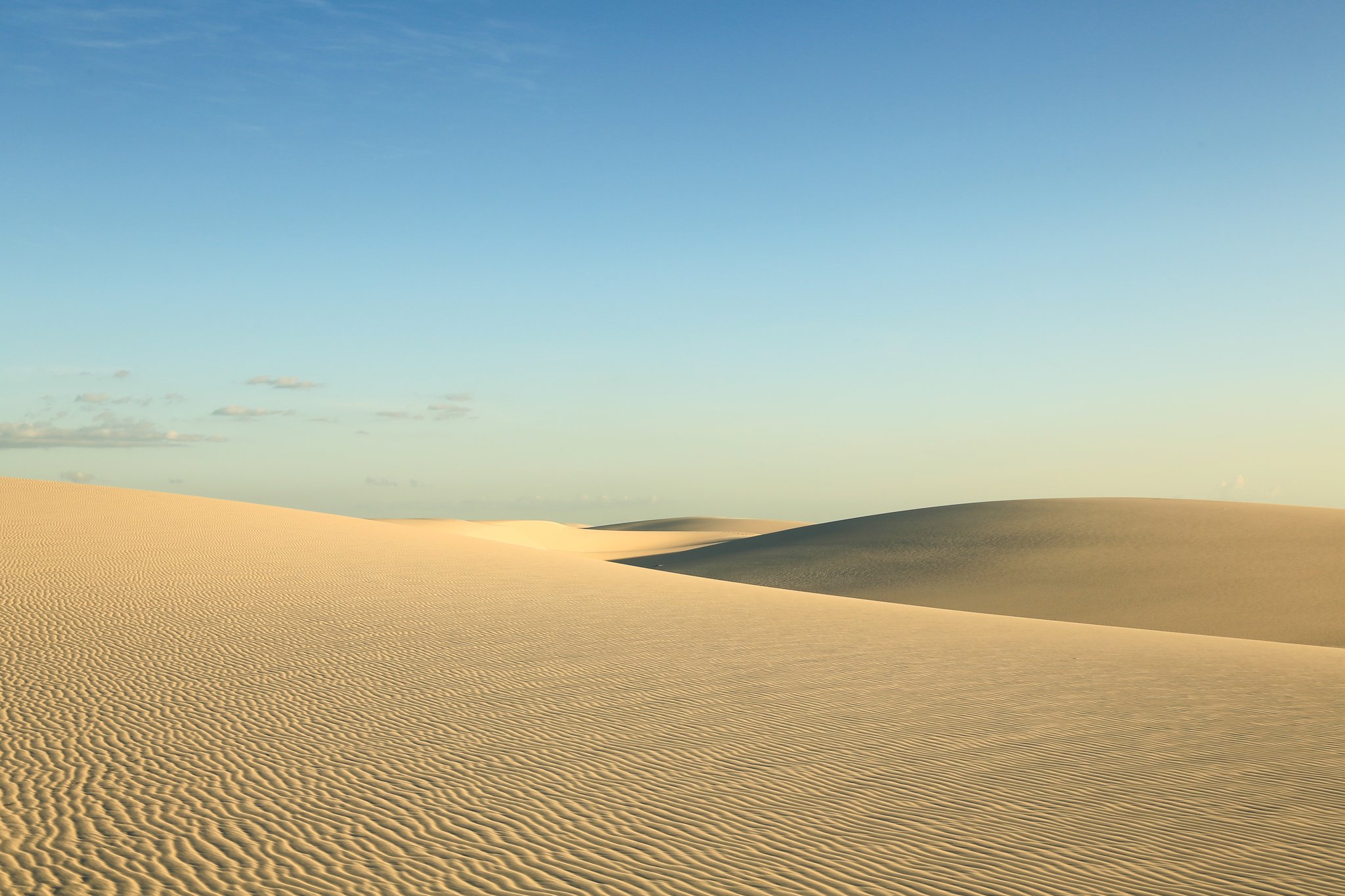 Wind-sculpted ridges, pure silence — the dunes at their most elemental. Photo: Brunomsbarreto Vast white sand dunes under a clear blue sky along the Lençóis Maranhenses hike, with wind-rippled ridgelines stretching to the horizon