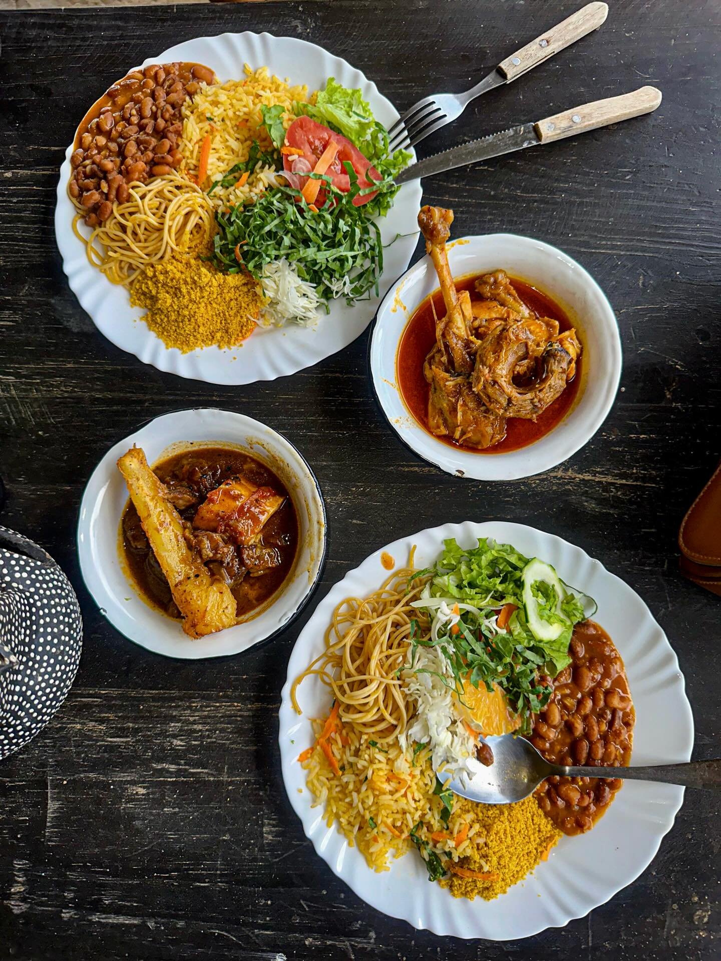 A generous spread of Maranhão home cooking, ready to fuel the next dune walk. Two large white plates loaded with rice, noodles, beans, farofa, and fresh salad alongside bowls of braised meat in rich sauce, served at a local restaurant near Lençóis Maranhenses Santo Amaro