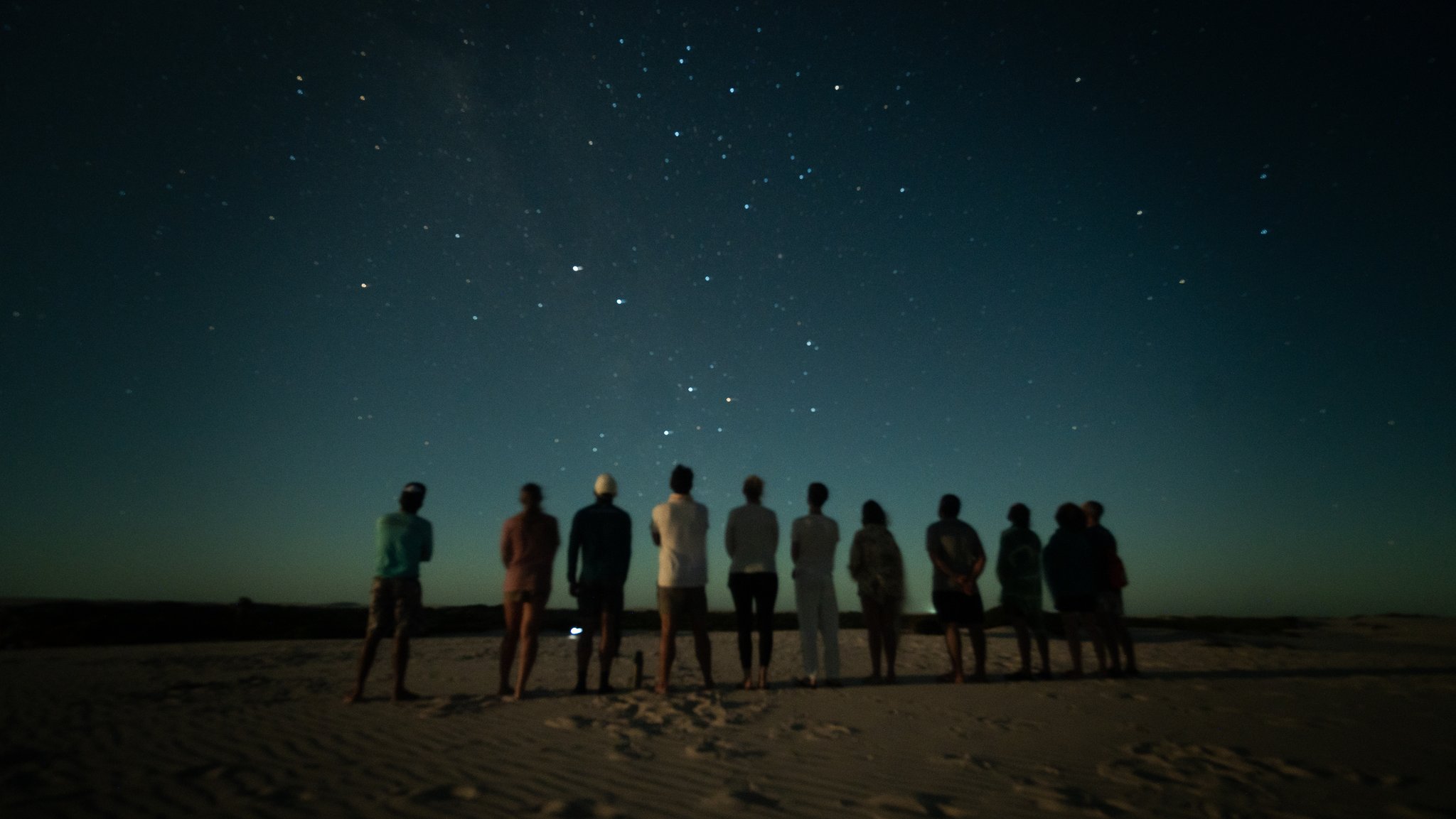 A group of travellers standing in a line on a sandy expanse, silhouetted against a star-filled night sky on a Lençóis Maranhenses trip