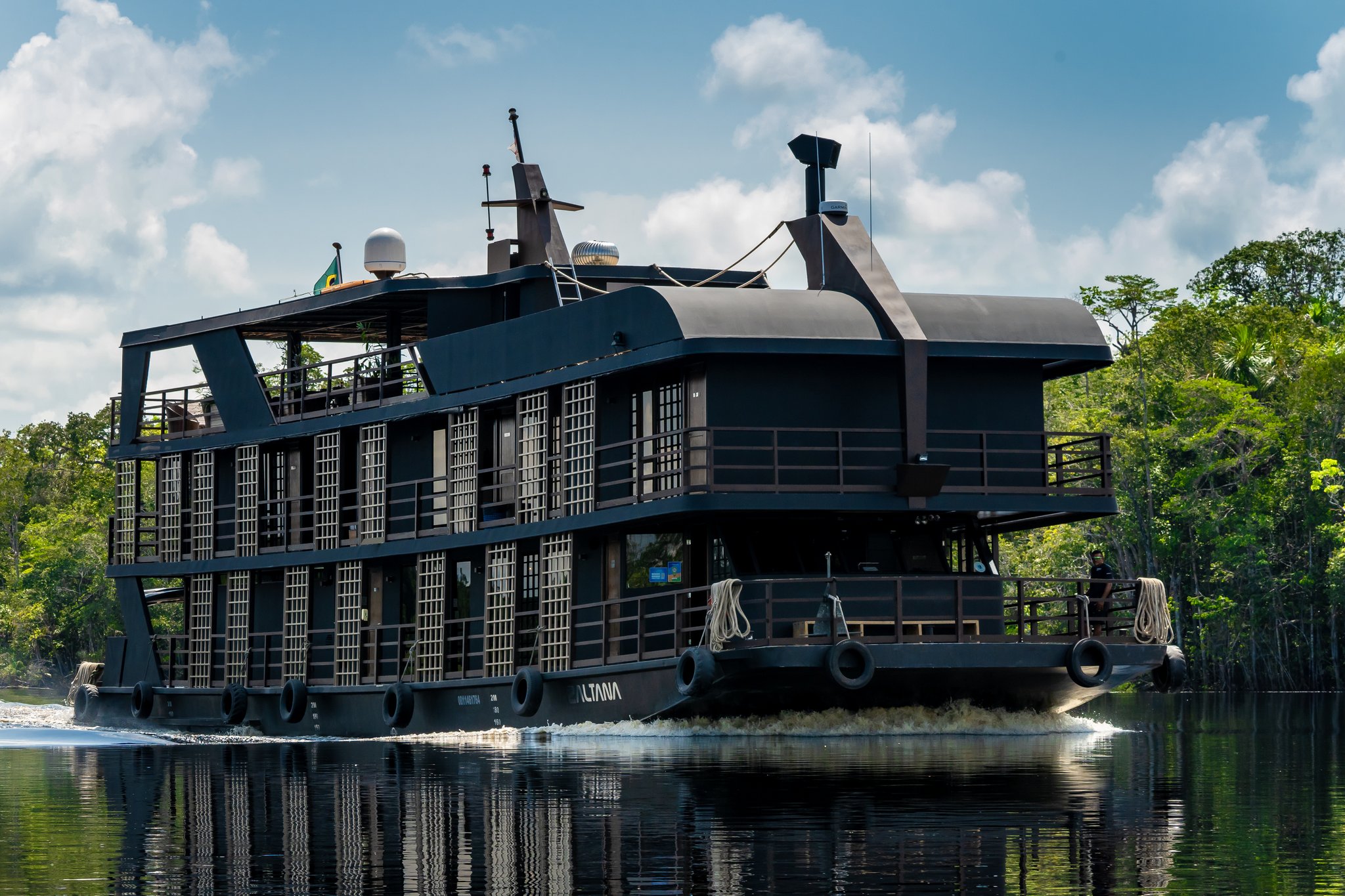 The Zaltana riverboat navigating a calm dark-water channel on a luxury Amazon cruise in Brazil, surrounded by dense rainforest under a partly cloudy sky
