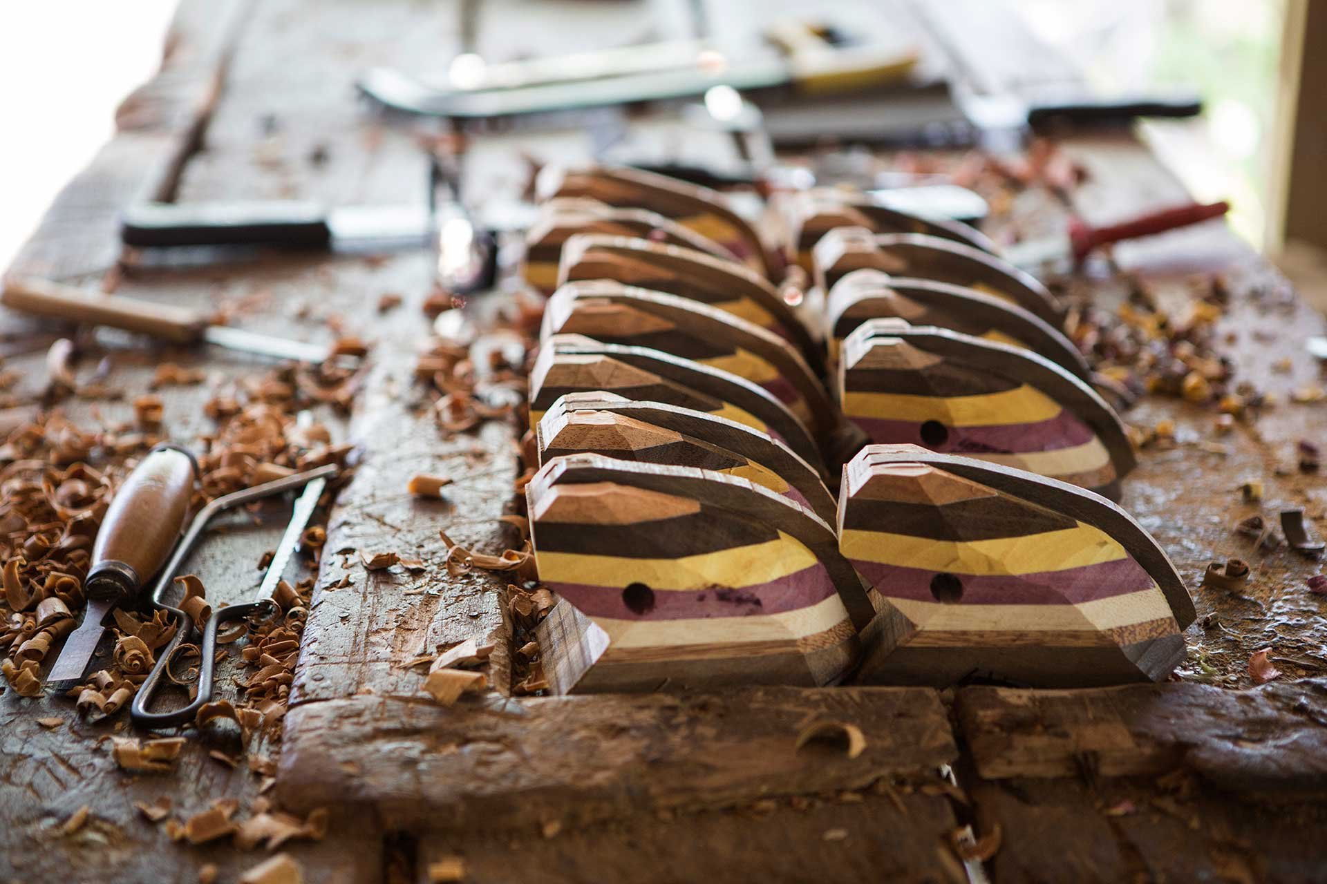Striped wood, curling shavings, carving tools — craftsmanship alive in the Amazon. Rows of handcrafted multicoloured laminated wood pieces in progress on a workbench scattered with shavings and carving tools, reflecting the artisan handicraft culture near this luxury amazon lodge brazil
