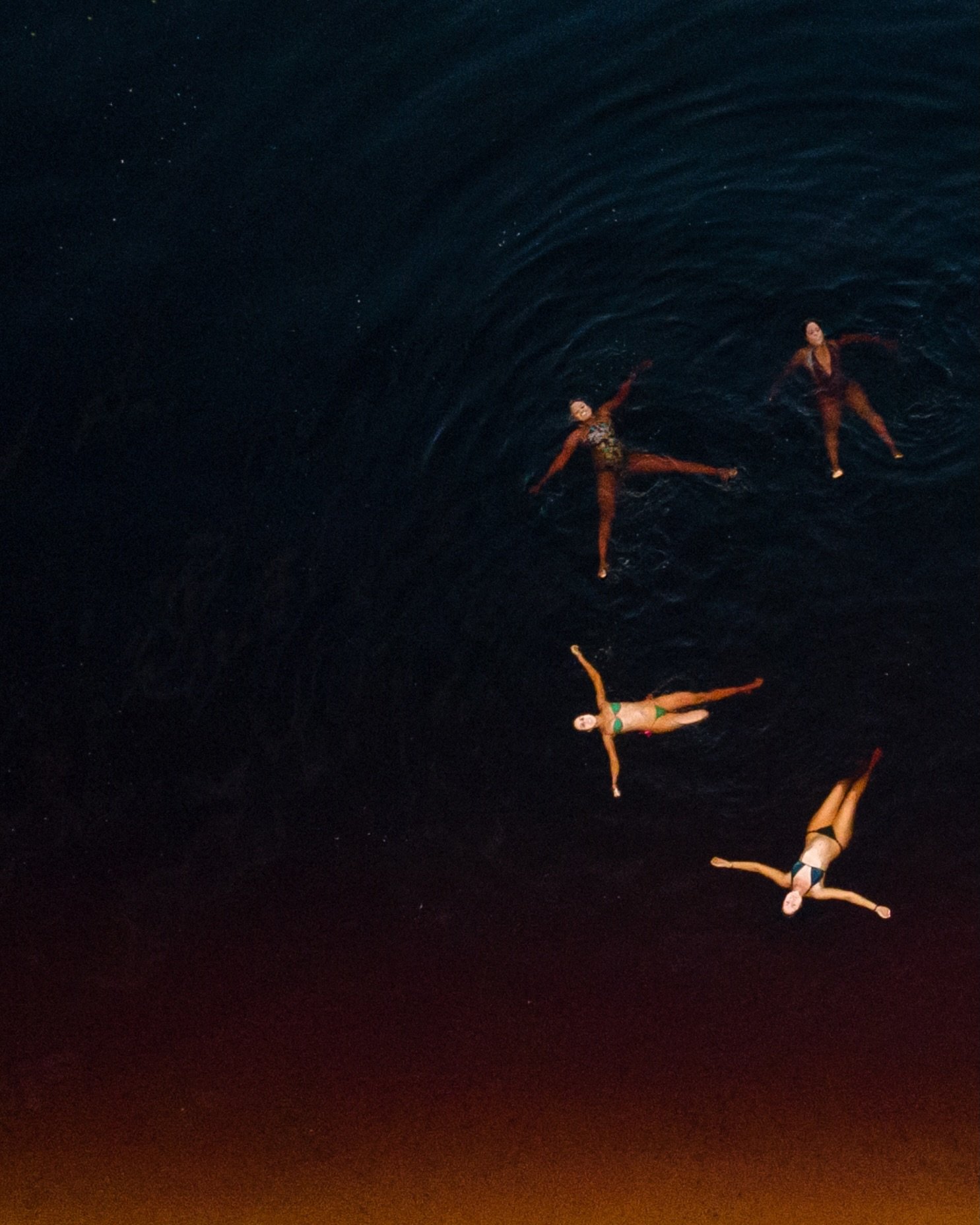 Four figures, arms outstretched, surrendered to the Rio Negro's obsidian depths. Aerial view of four swimmers floating on their backs in the dark tannin-rich waters of the Rio Negro, part of a luxury Amazon lodge Brazil experience