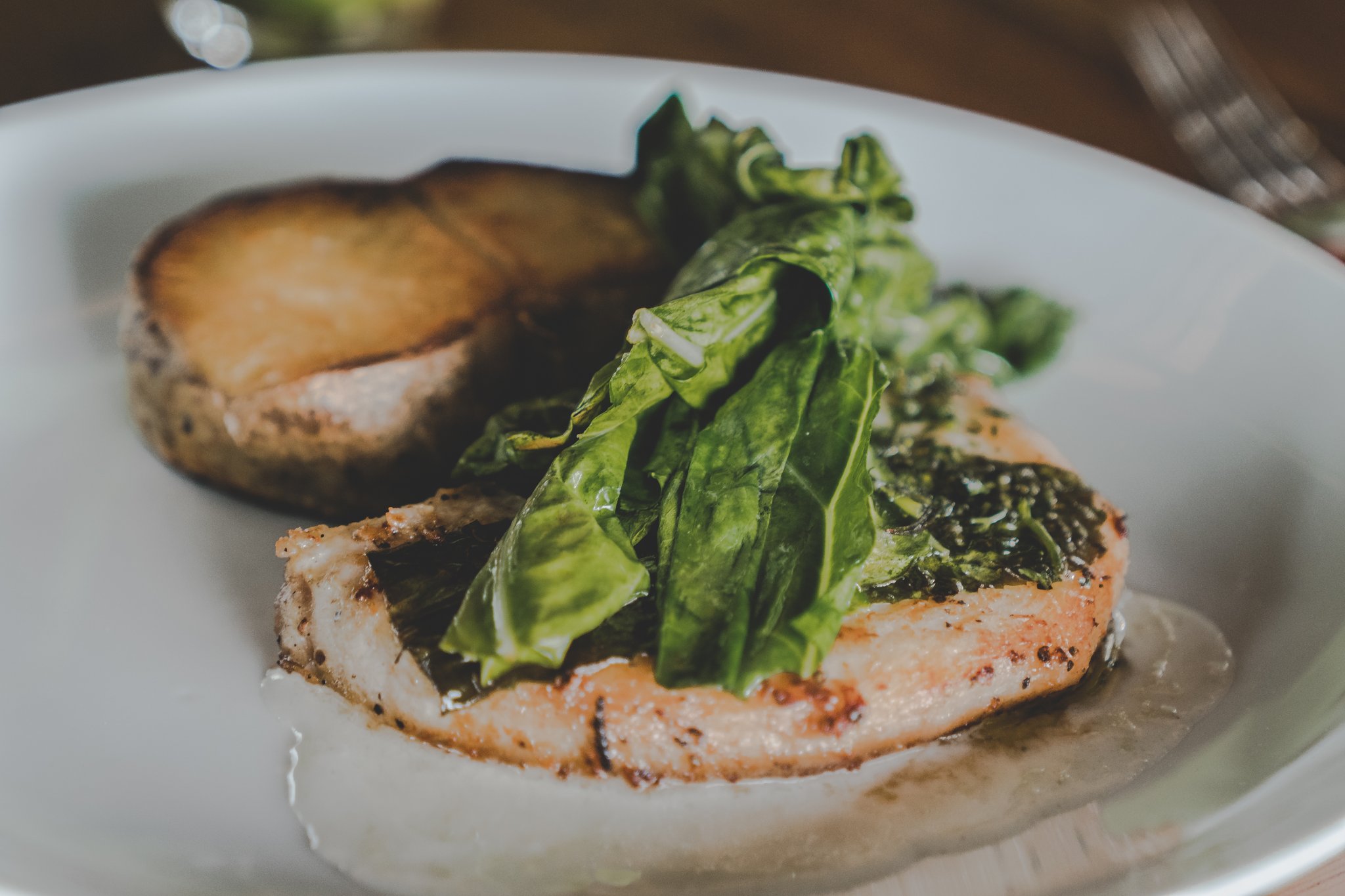 Local catch, simply plated — the Amazon on a plate. Pan-seared fish fillet topped with fresh green leaves served on a white plate with a roasted portobello mushroom at a luxury Amazon lodge Brazil restaurant