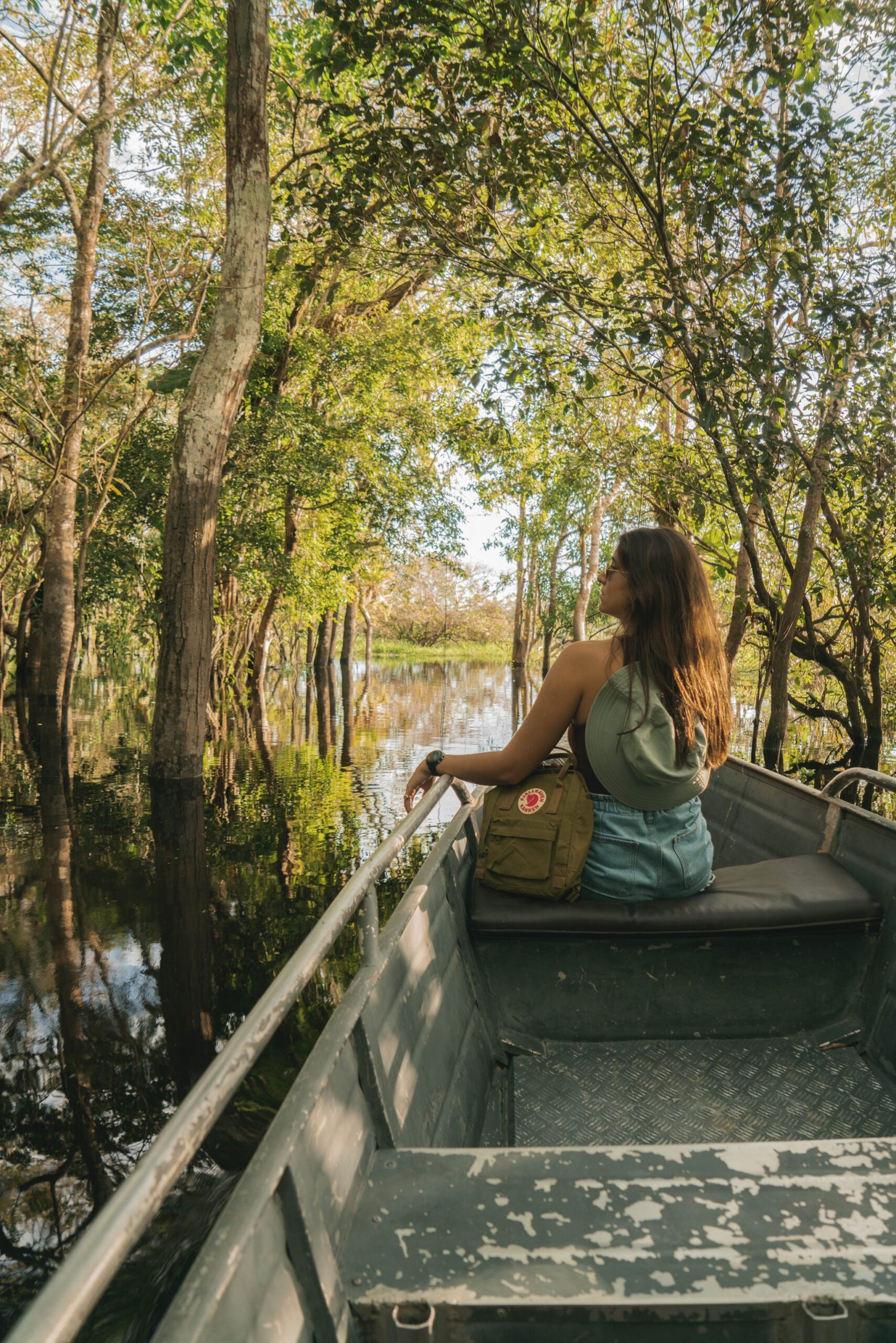 Gliding quietly through the flooded forest, every bend a new discovery. Photo: Yuri Panichi A traveller sits on the bow of a metal boat during a Manaus jungle tour, gazing into a sun-dappled flooded forest with trees rising from still, reflective water