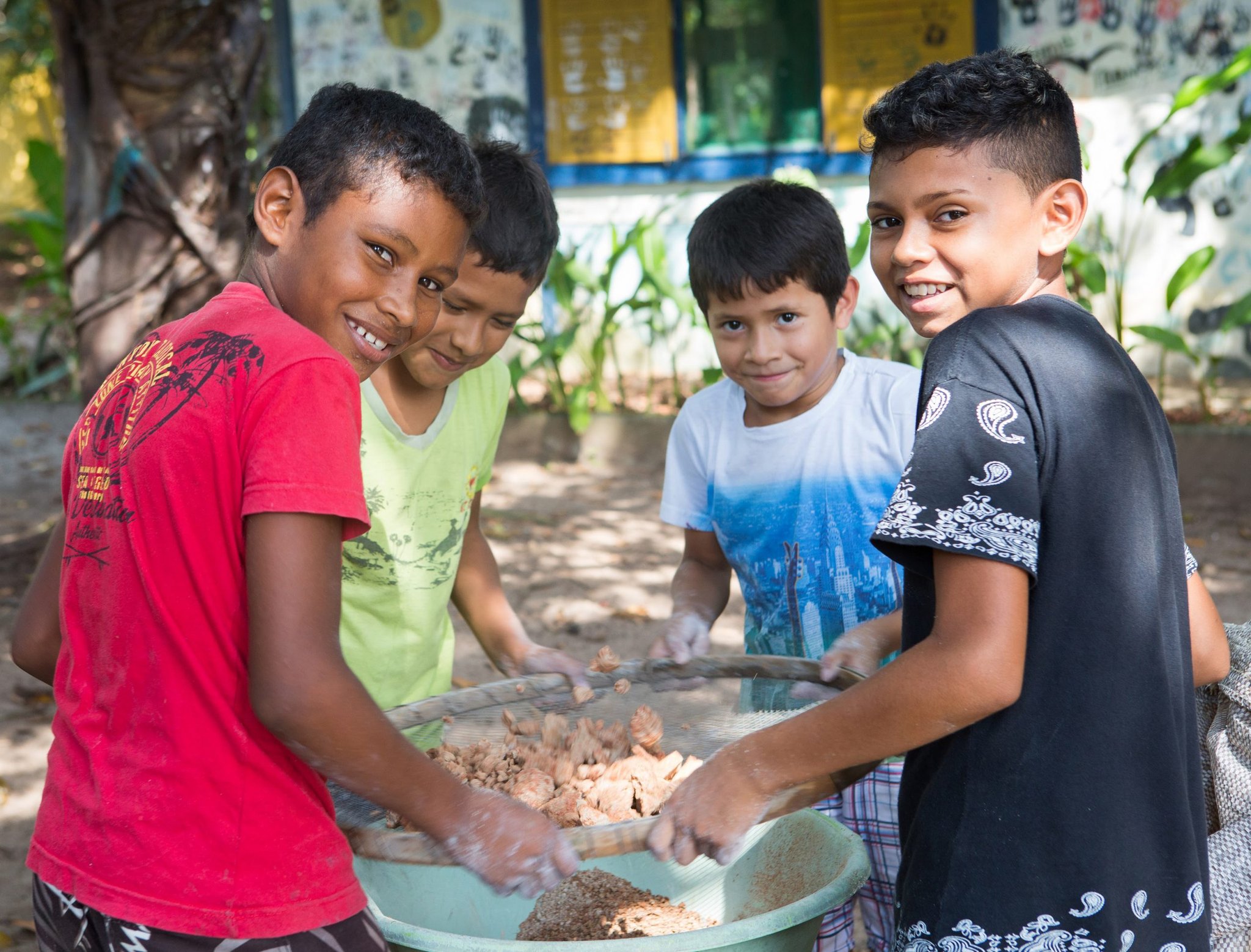 Hands-on and heartfelt — local kids share their daily rhythms with visitors. Four smiling boys work together sifting food in a large bowl during a visit to a riverside community near Mirante do Gavião in the Amazon