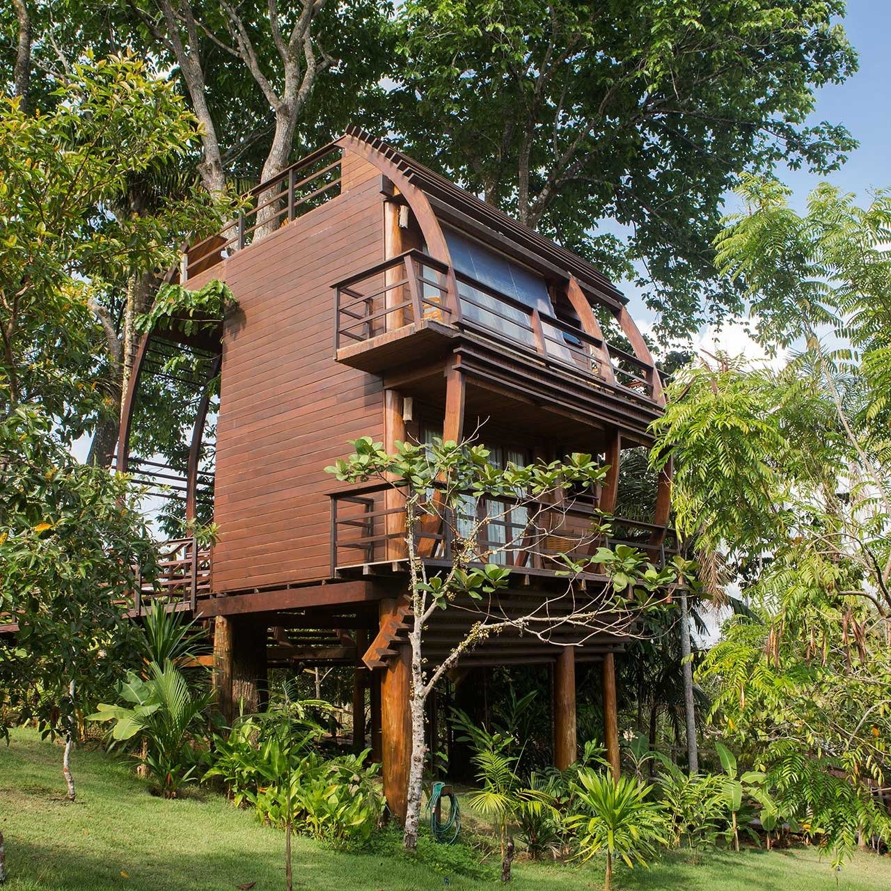 Sleep among the canopy — the iconic treehouse at Mirante do Gavião. Multi-storey wooden treehouse at Mirante do Gavião rising on stilts above lush Amazonian garden vegetation