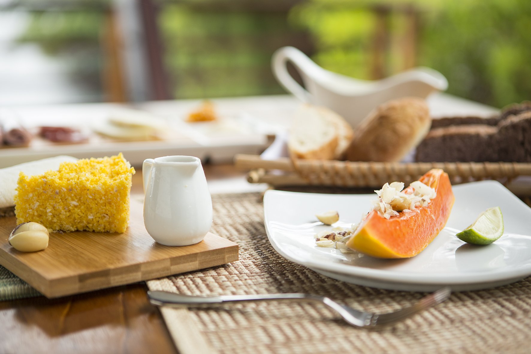Mornings in the Amazon, served fresh. Fresh papaya topped with coconut and nuts, yellow cornbread on a bamboo board, and artisan bread served on an outdoor table at Mirante do Gavião