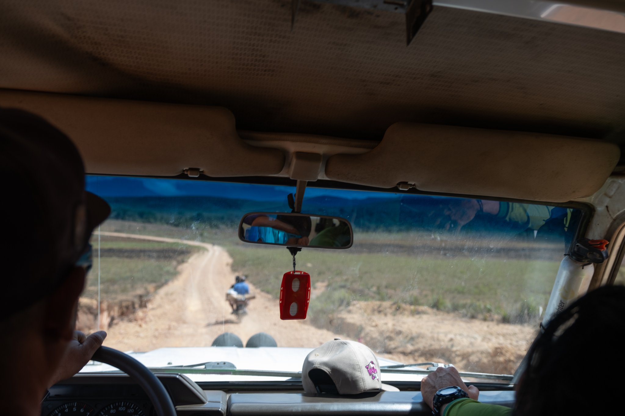 View from inside a 4x4 vehicle following a motorcycle along a winding dirt road through open grassland on the Mount Roraima hike approach