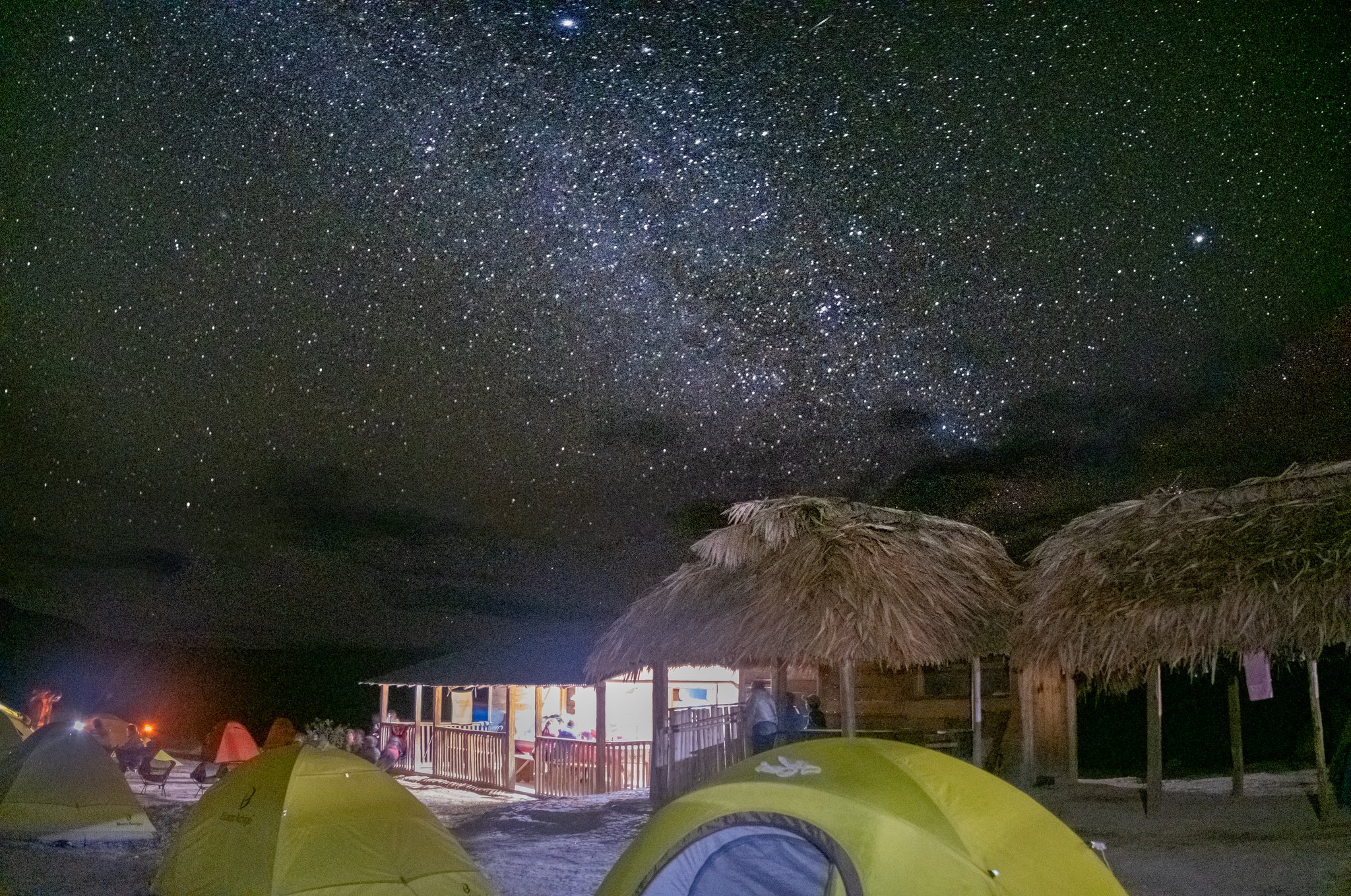 Green dome tents and thatched-roof shelters lit up at night on the Mount Roraima hike, with the Milky Way stretching across a dark sky above