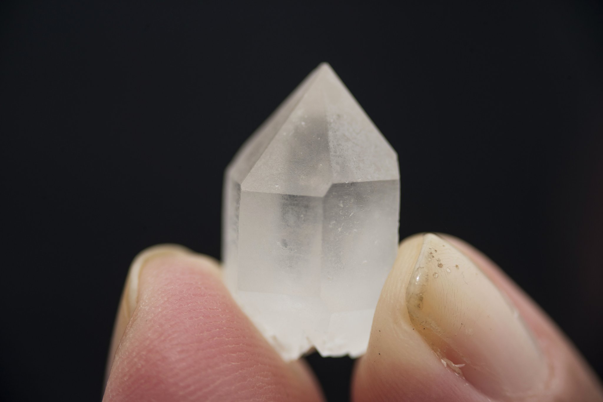 A small clear quartz crystal point held between two fingers against a black background, found in the Valley of Crystals on the Mount Roraima hike