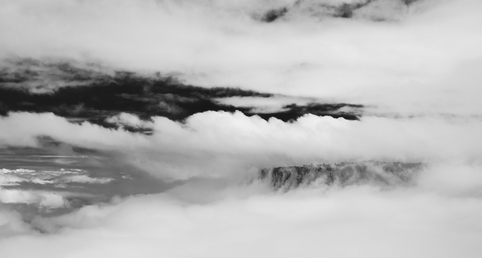 A rocky tepui cliff face barely visible through thick swirling clouds during a Mount Roraima trek, captured in dramatic black and white
