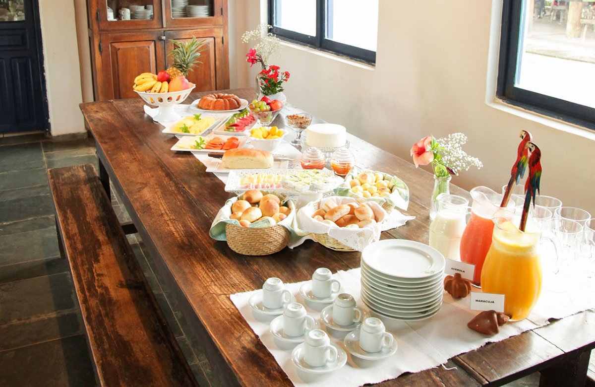 Tropical fruits, fresh-baked rolls and pitchers of maracujá juice — mornings done right. Photo: Alexis Prappas - www.prappas.com A generous Brazilian breakfast buffet laid on a rustic wooden table on a Pantanal Bonito tour, featuring fresh tropical fruits, bread rolls, cakes, acerola juice, maracujá juice and espresso cups