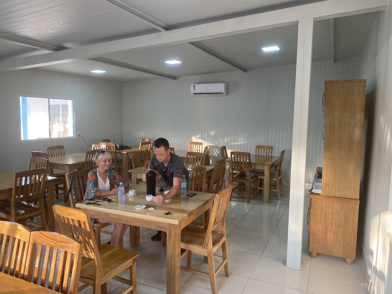 A quiet coffee break before the next wildlife adventure begins. Two travellers sharing coffee at a wooden table inside a clean, air-conditioned dining room on a pantanal jaguar budget safari