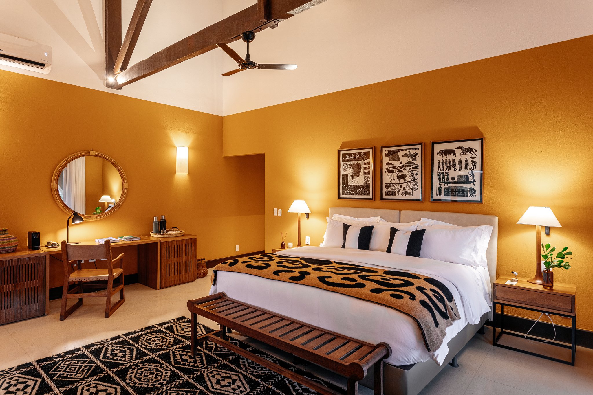 Ochre walls, handwoven textiles, and local folk-art prints — rest that feels rooted in the land. Photo: Felipe Castellari Sun-warmed ochre walls, exposed timber ceiling beams, and folk-art prints above the king bed in a pantanal luxury safari lodge room