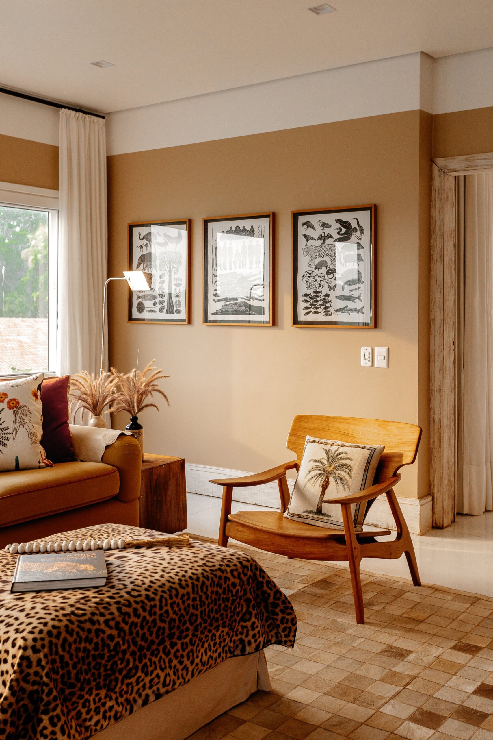 Animal prints, handcrafted timber, and framed wildlife art — every detail tells the story of the Pantanal. Photo: Felipe Castellari A warmly decorated suite at Caiman Ecological Refuge featuring a leopard-print bedspread, mid-century timber armchair with a palm-motif cushion, and three framed wildlife illustrations on ochre walls — embodying pantanal luxury safari style