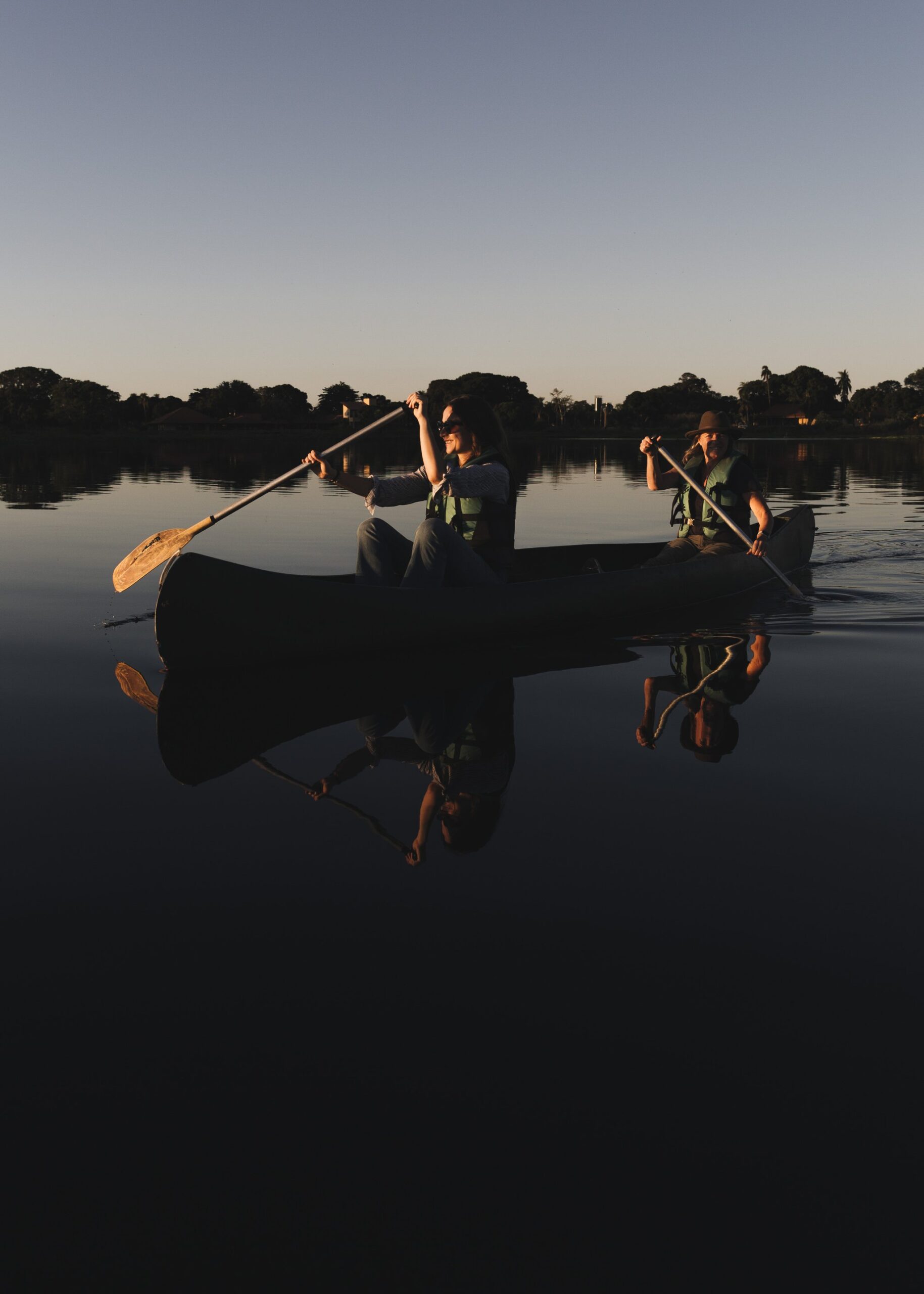 Perfectly still water, two paddles, and a fading sky — some evenings simply refuse to be rushed. Two guests in life vests paddle a canoe across mirror-still water at dusk on a pantanal luxury safari, their reflections perfectly mirrored on the glassy surface