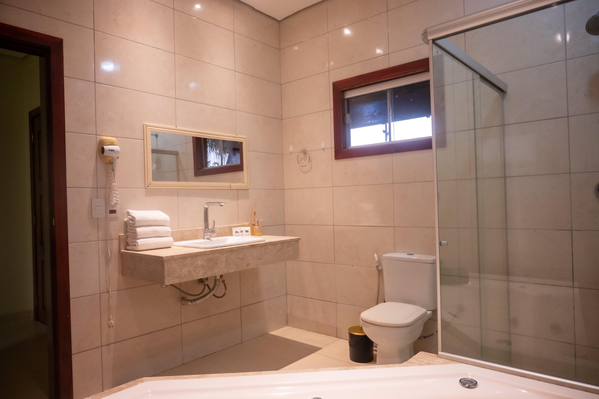 Clean, spacious, and fully equipped — comfort waiting after a long day in the wild. Spacious private bathroom at a Pantanal Tour from Cuiabá lodge, featuring a marble-finish vanity, folded white towels, glass-enclosed shower, bathtub, and a wall-mounted hair dryer
