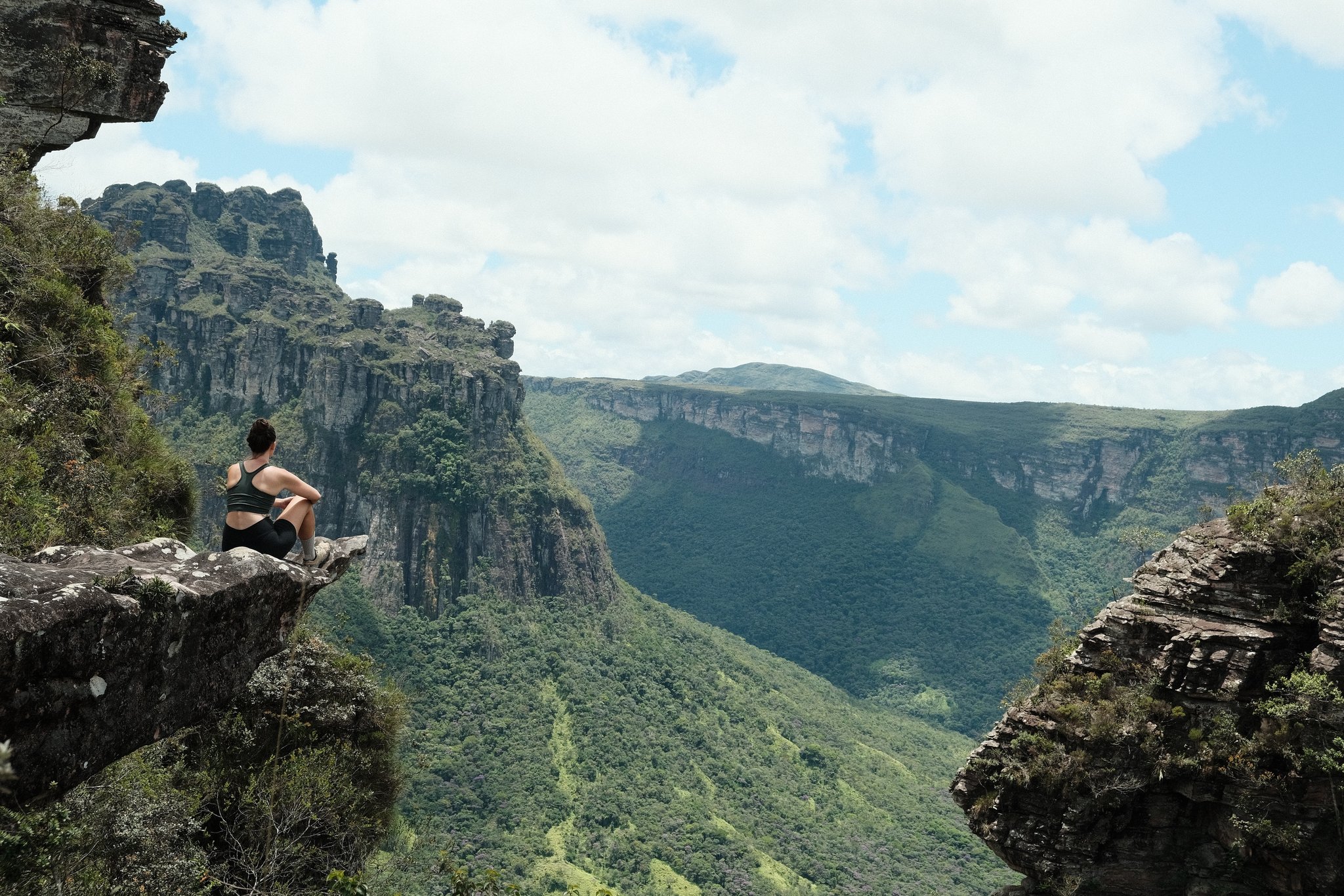 Sandstone giants, silence, and nowhere else to be. A hiker sits alone on a rock ledge overlooking a vast green canyon during the Pati Valley hike, with towering sandstone cliffs and forested valley walls stretching into the distance under a partly cloudy sky