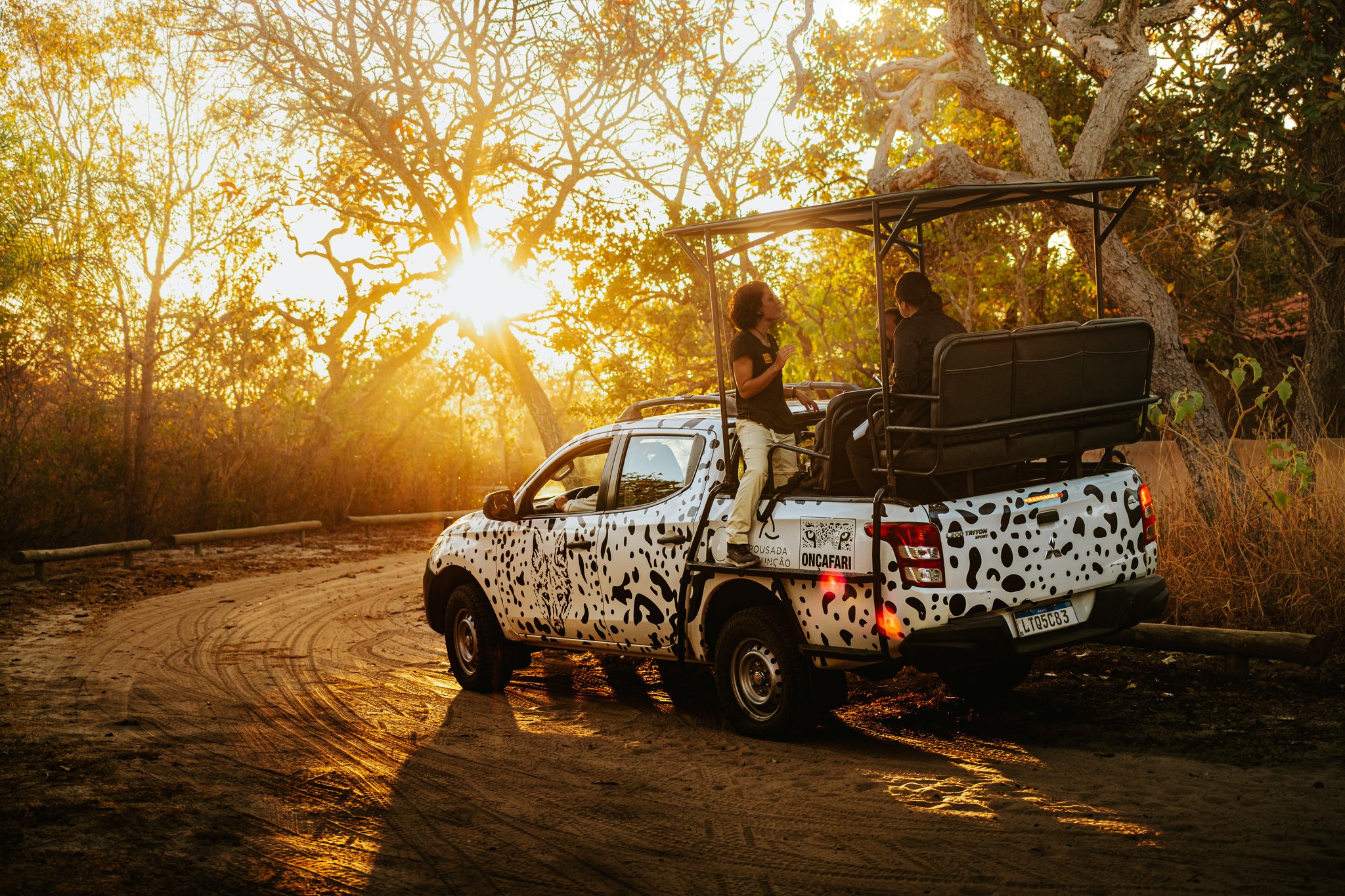 Oncafari jaguar-spotted safari truck with guests on board paused on a dirt track at golden-hour sunset in the Cerrado at Pousada Trijunção