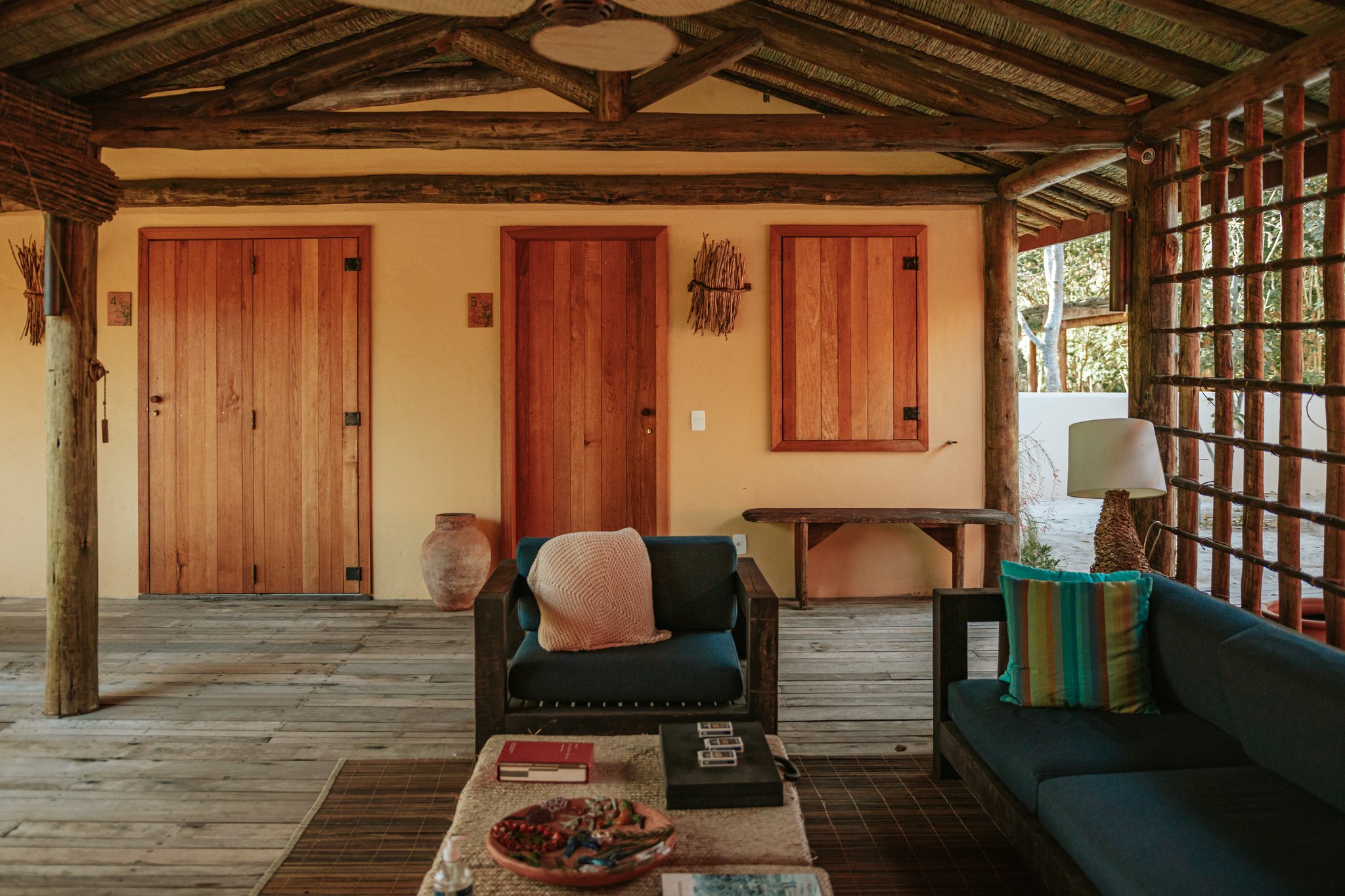 Open-air covered veranda at Pousada Trijunção with teal armchairs, wooden log pillars, warm terracotta walls and handcrafted wooden doors