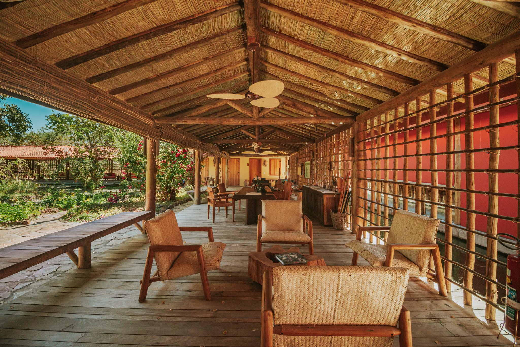 Open-air lounge terrace at Pousada Trijunção with woven rattan chairs, rustic wooden deck, thatched palm roof and a lush garden view