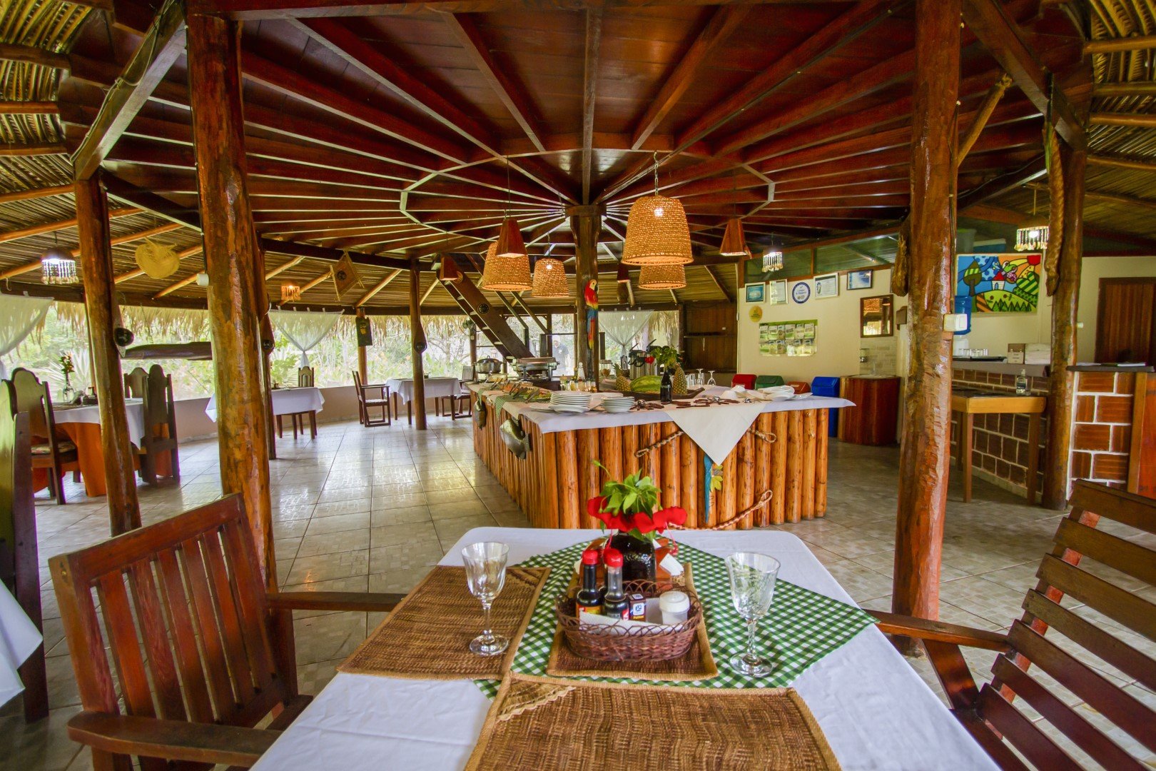 Rustic timber dining pavilion with set tables and a central buffet under a high wooden roof at a jungle lodge