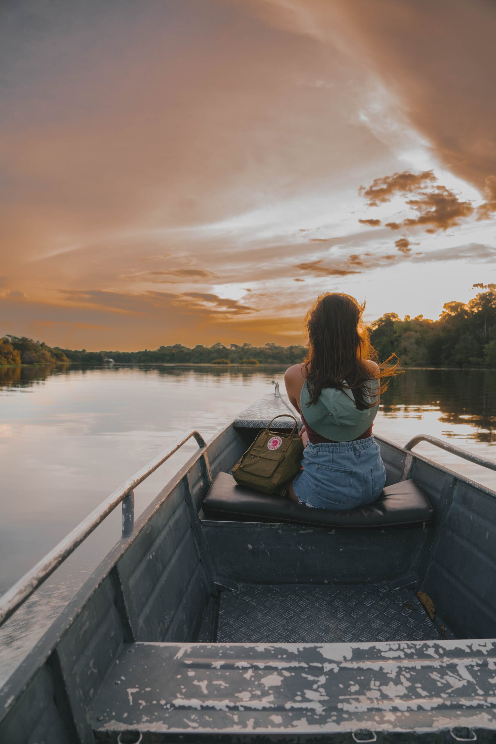 The first evening sets the tone: a glowing sunset welcomes you from the river. Photo: Yuri Panichi Traveler watching a golden sunset from the bow of a boat on arrival in the Amazon