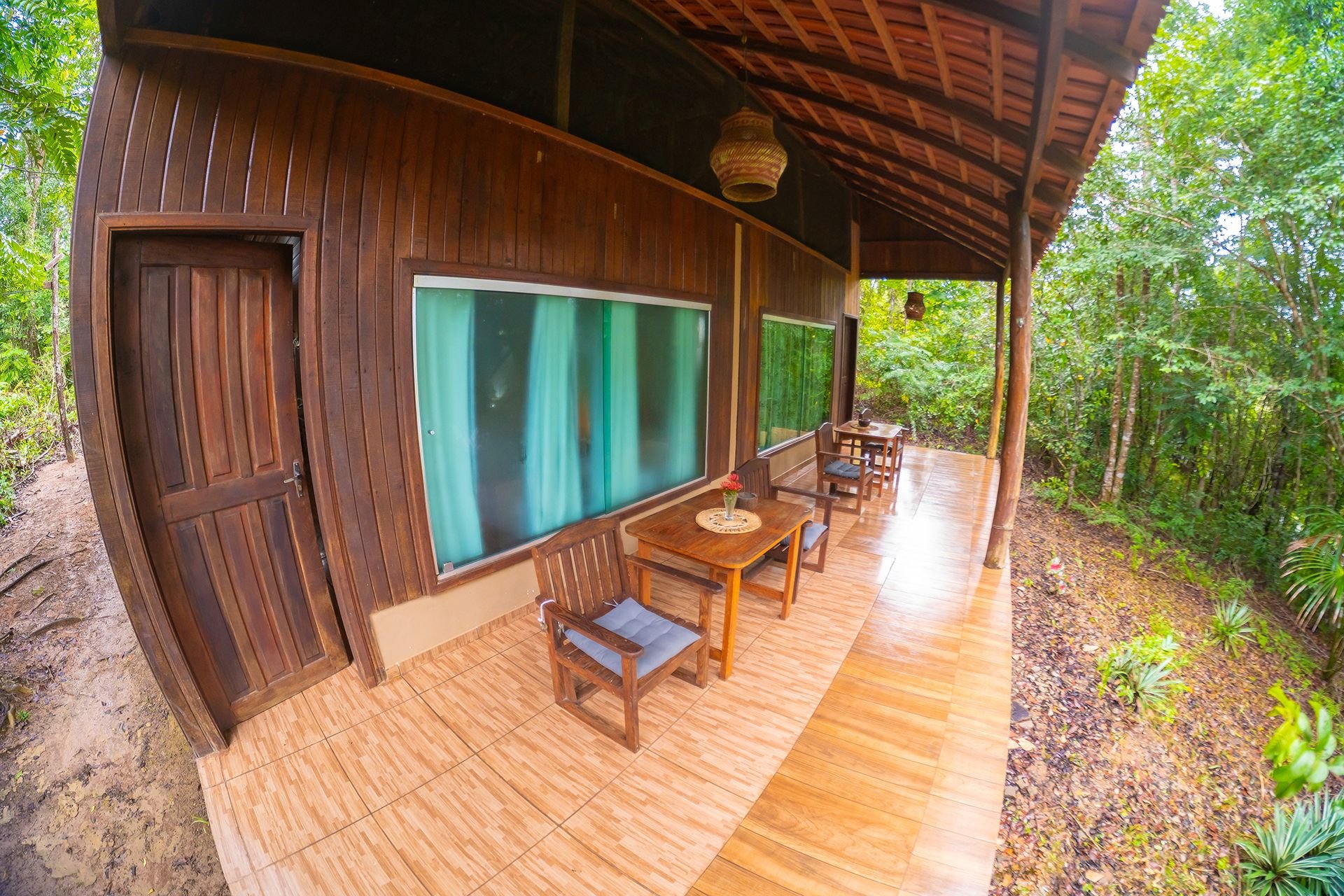 The superior bungalow's long veranda opens straight onto the forest. Wooden veranda of a superior bungalow with chairs running along the forest side in the Amazon