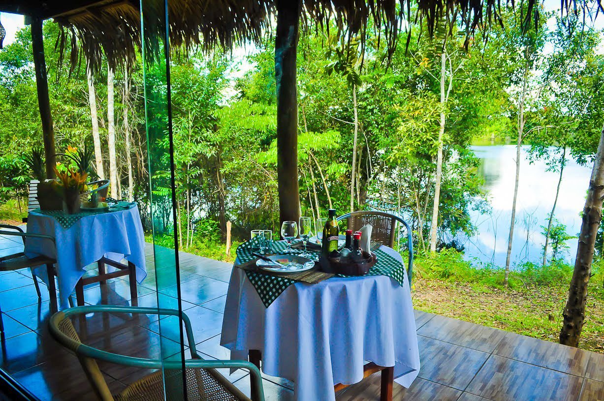 Set dining tables on a covered terrace at Turtle Lodge overlooking a quiet forest lake