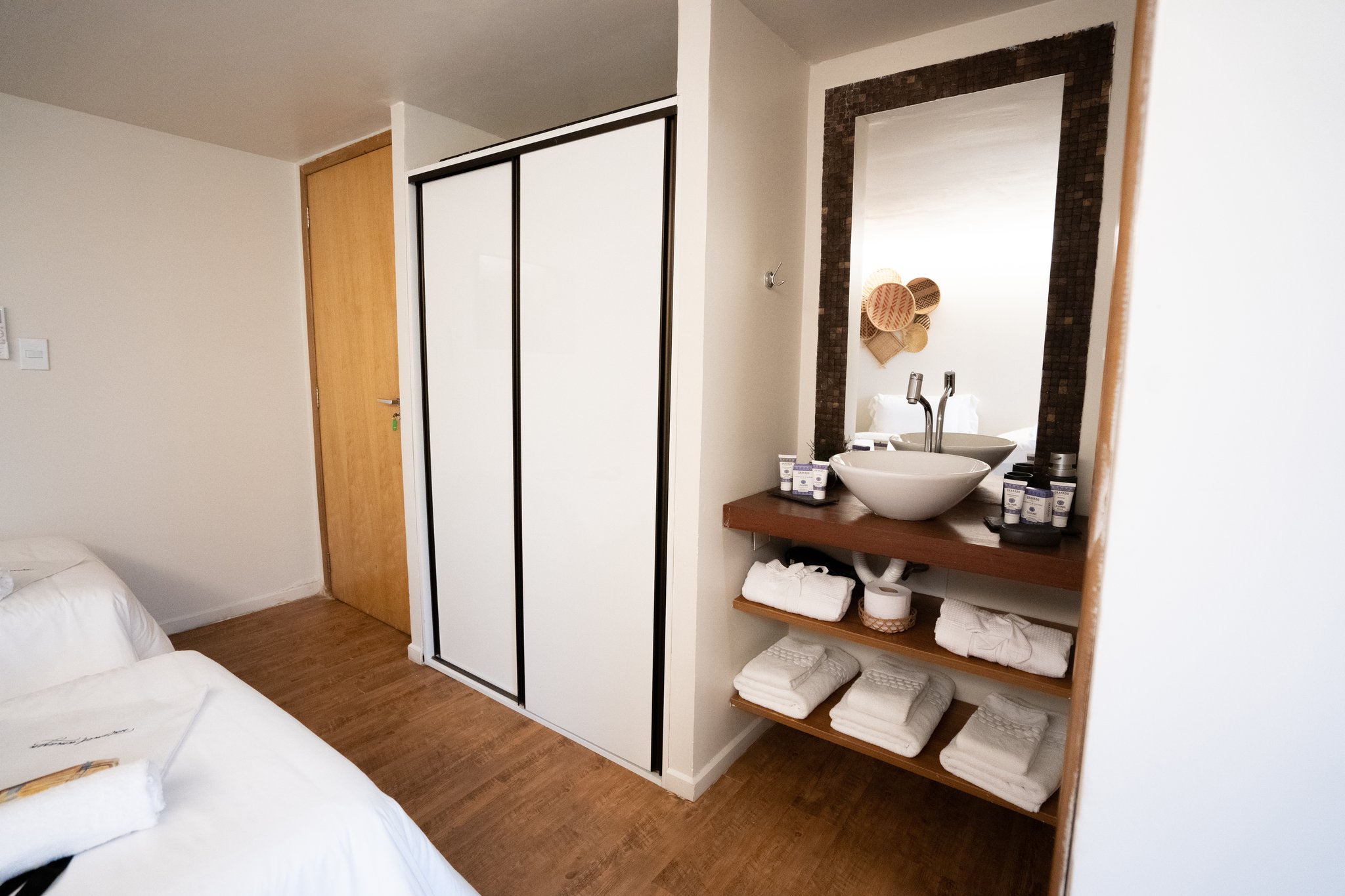 A neatly arranged vanity area on the untamed amazon cruise featuring a vessel-bowl sink on a wooden shelf, folded white towels, toiletries, and a mosaic-framed mirror beside a sliding-door wardrobe